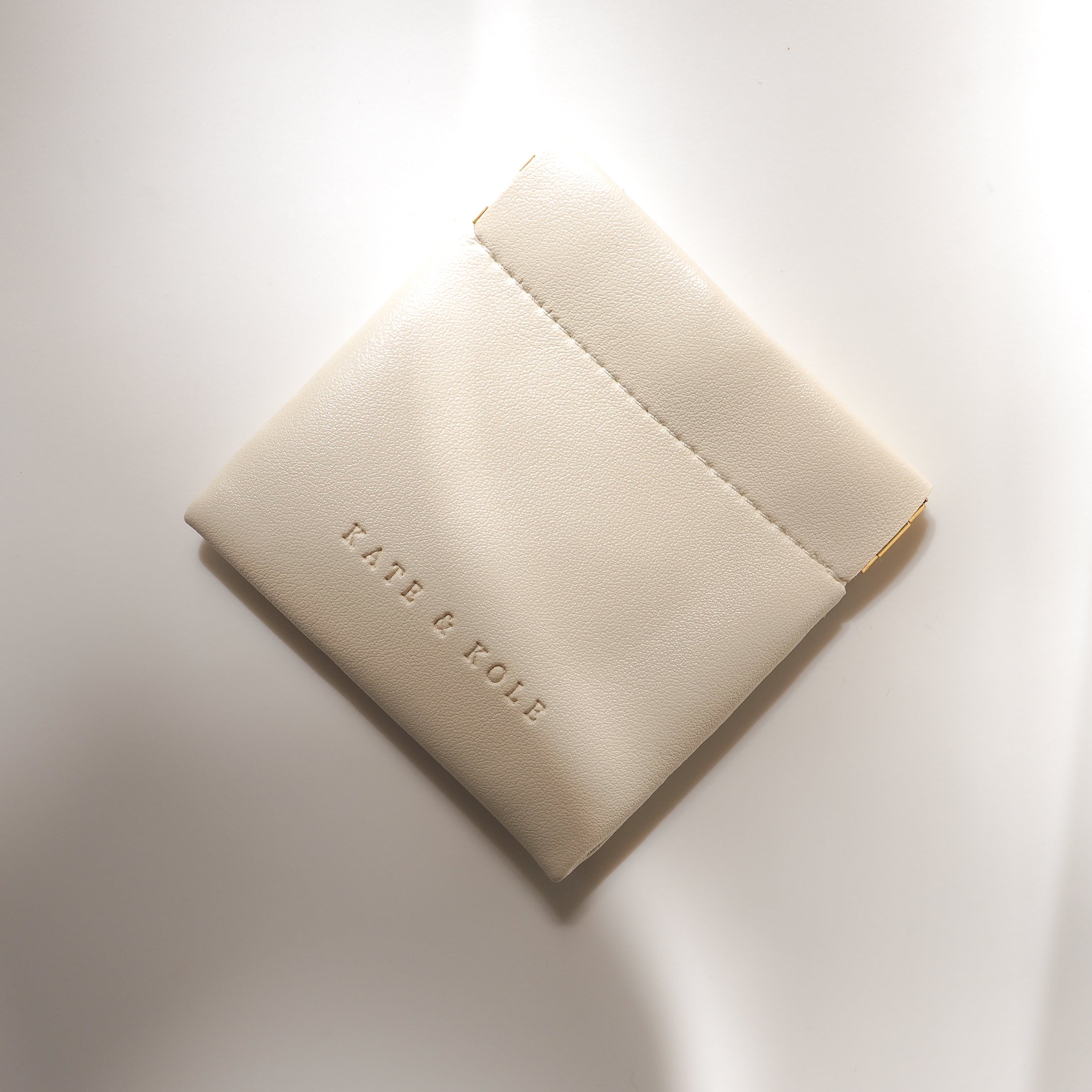 Elegant cream-coloured leather jewellery pouch with embossed "KATE & KOLE" branding, showcasing a luxurious and minimalist design.