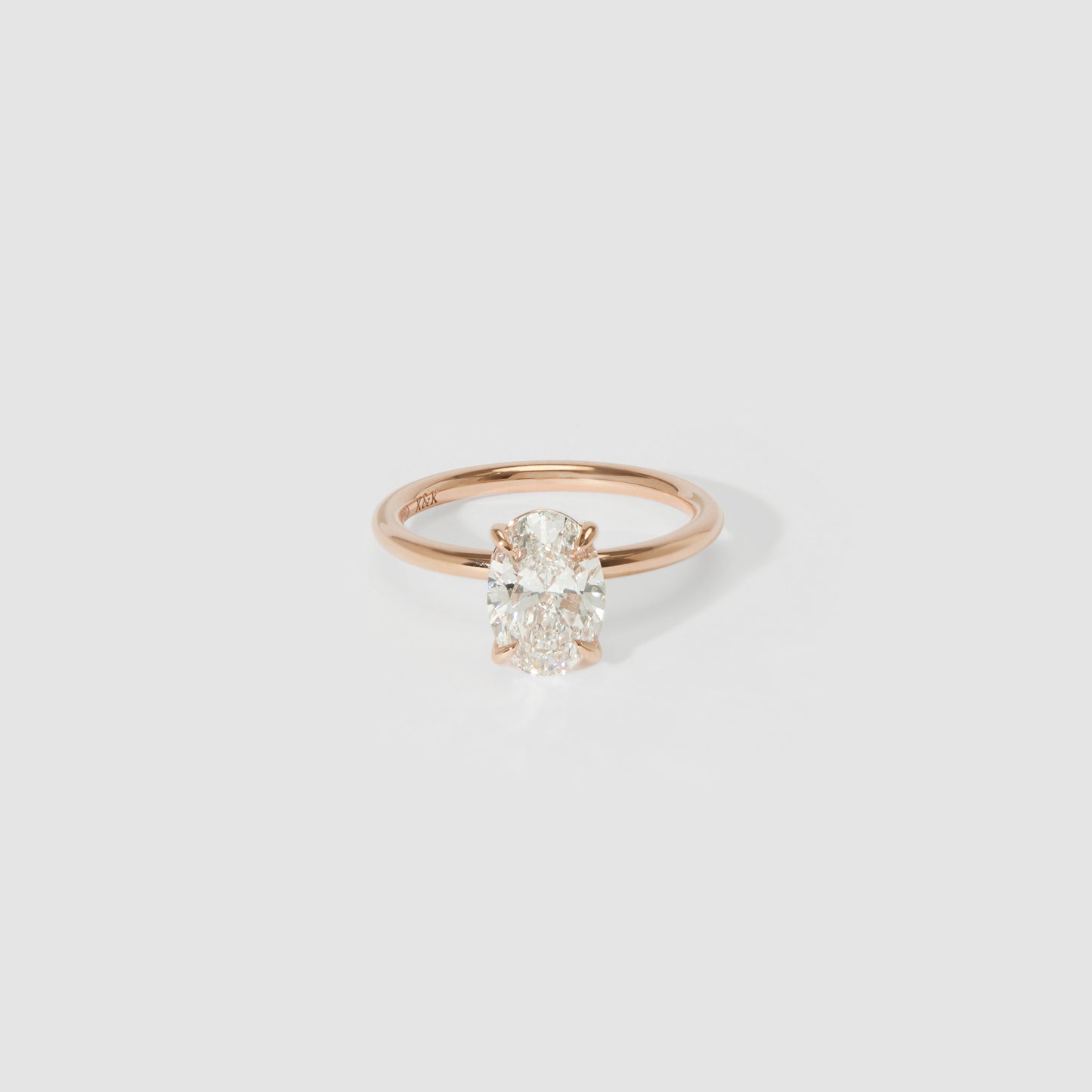 Oval diamond ring with a rose gold band, placed on a light grey background, highlighting luxury jewellery design.