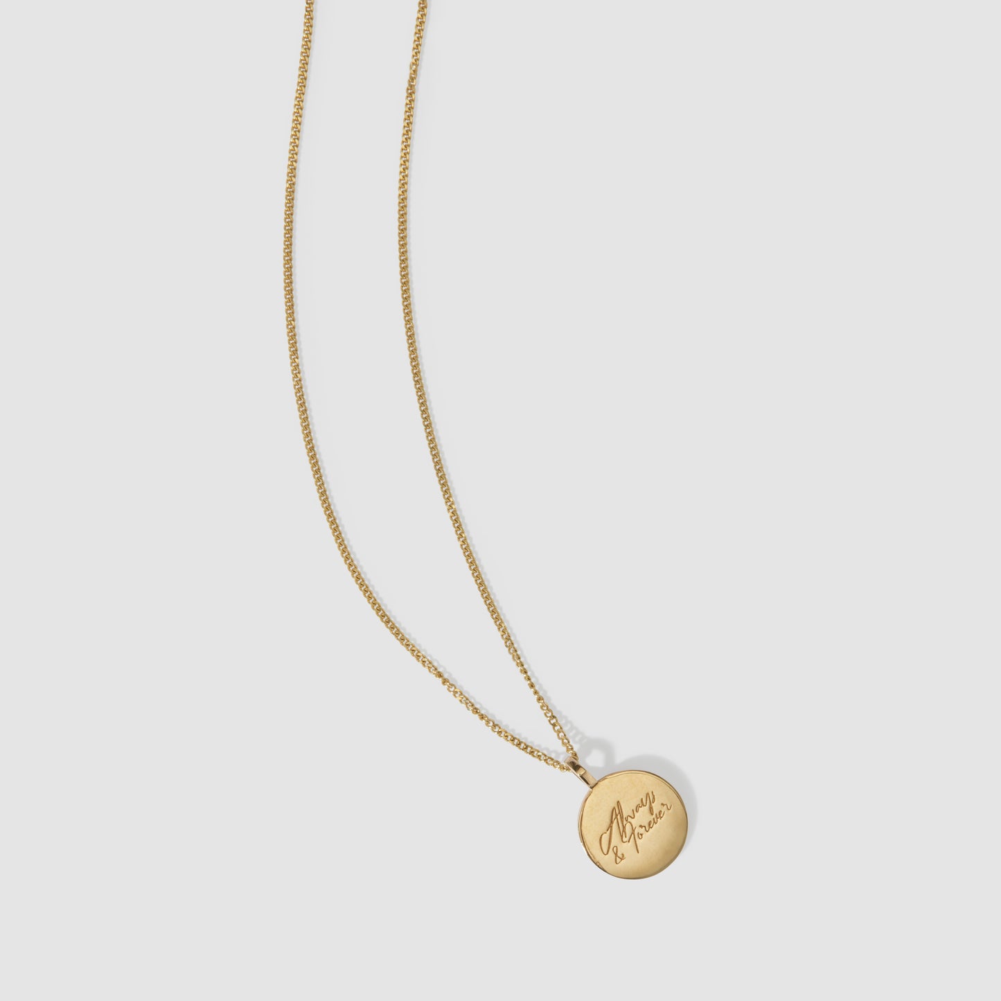 Gold necklace with a round pendant, engraved with cursive text, against a plain light grey background. Perfect for luxury jewellery lovers.