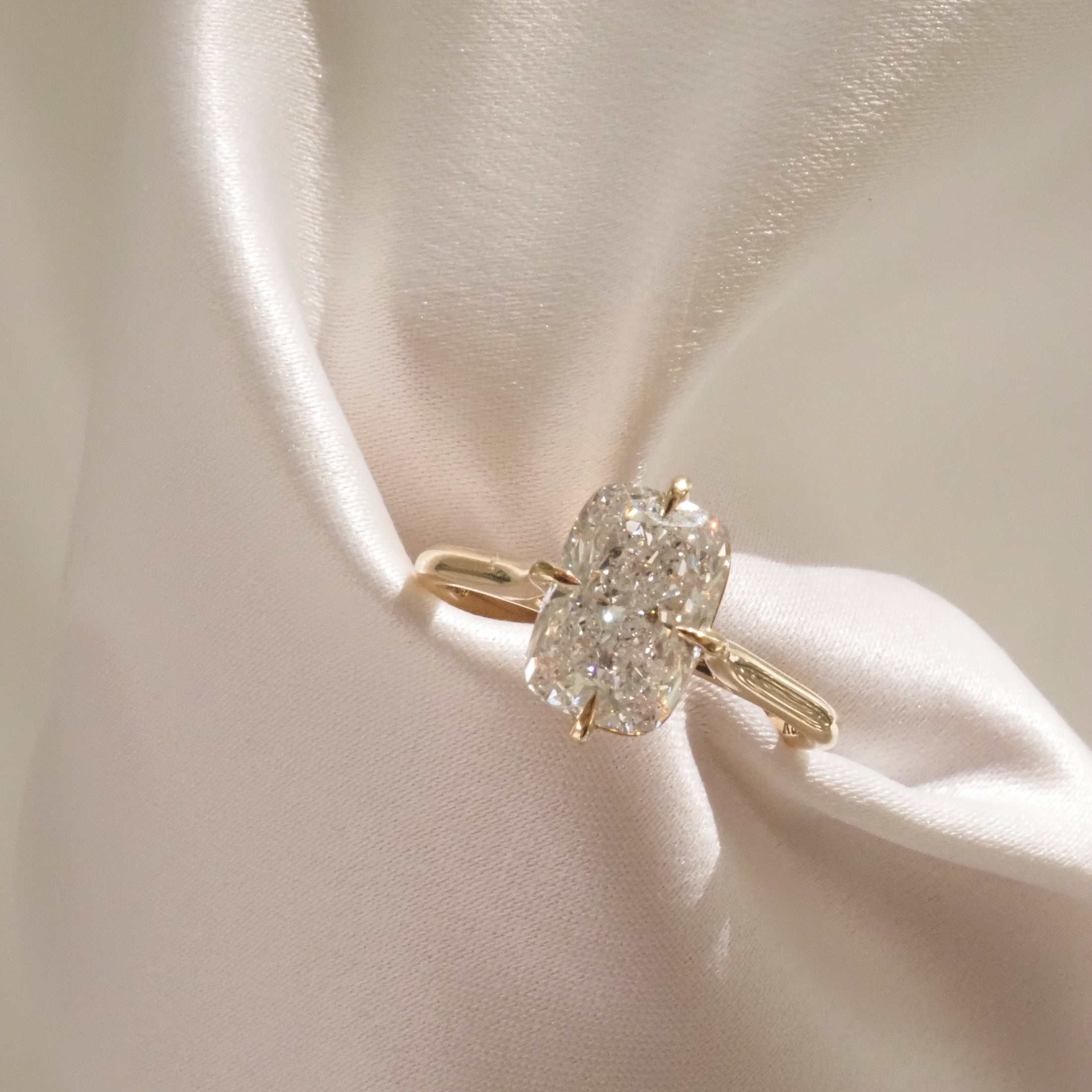 Elegant diamond ring with a cushion-cut centre stone set in gold, displayed on silky white fabric. Luxury jewellery glamour.