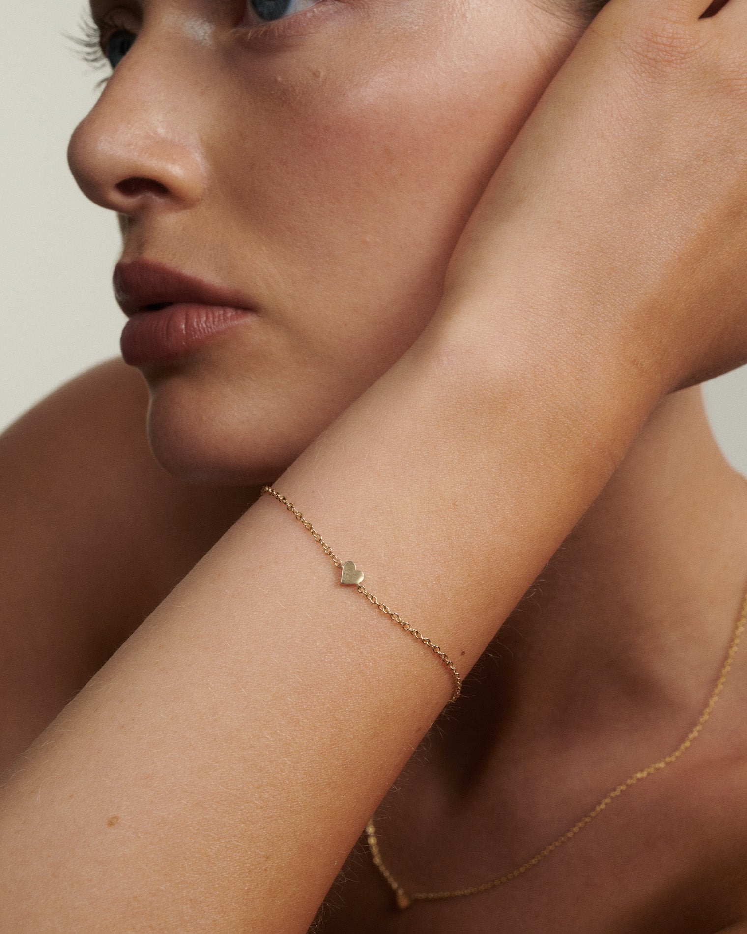 Close-up of a woman's arm wearing a delicate gold bracelet with a heart charm.