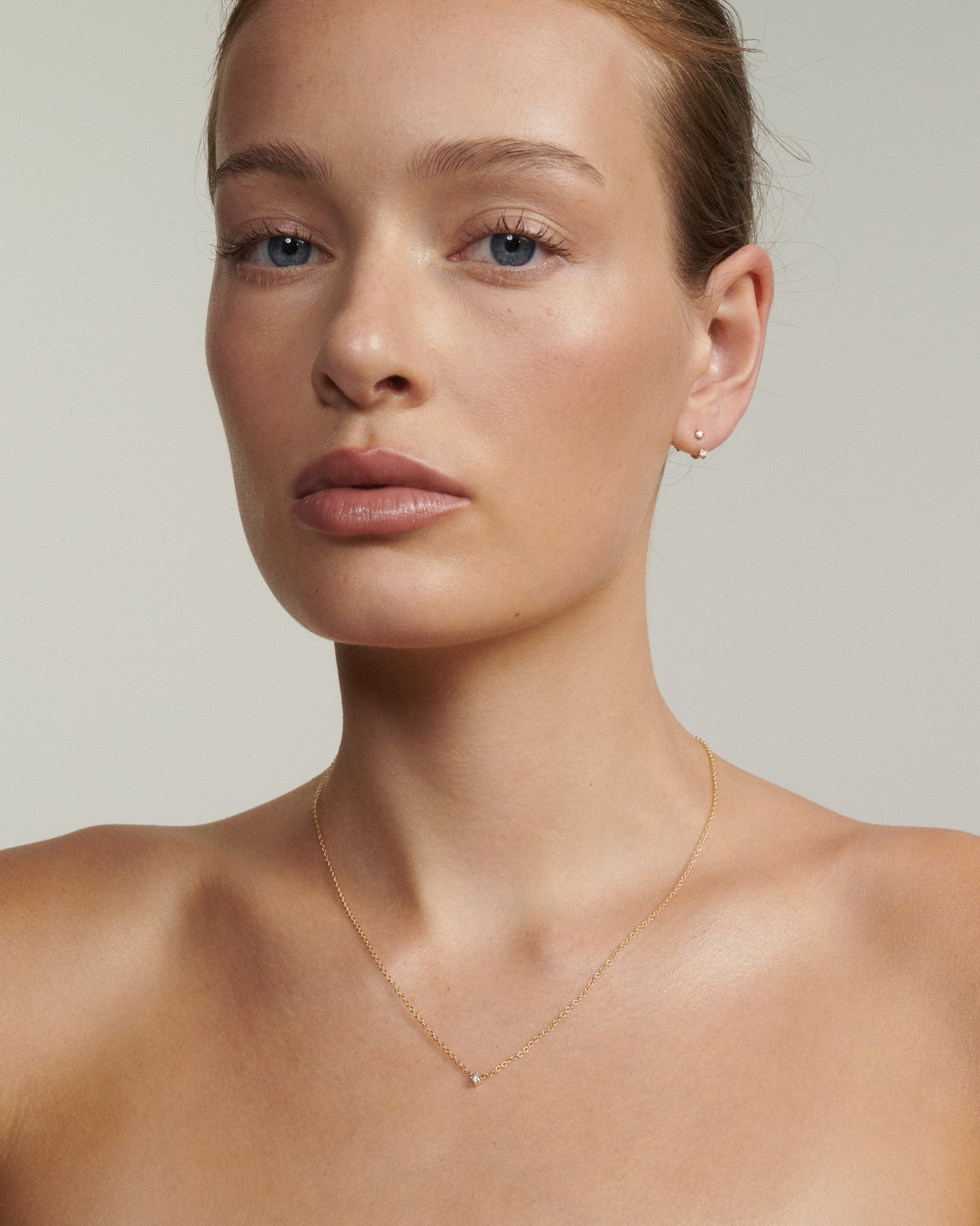 Close-up of a person wearing a delicate gold necklace and earrings against a neutral background