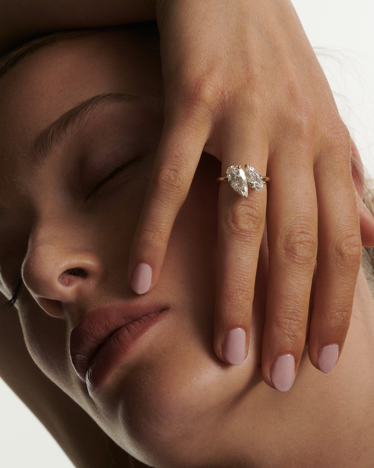 Close-up of a woman's face with a hand resting on her cheek, wearing a diamond ring.