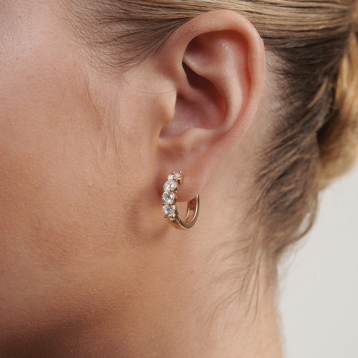 Close-up of an ear wearing a gold hoop earring with small stones.