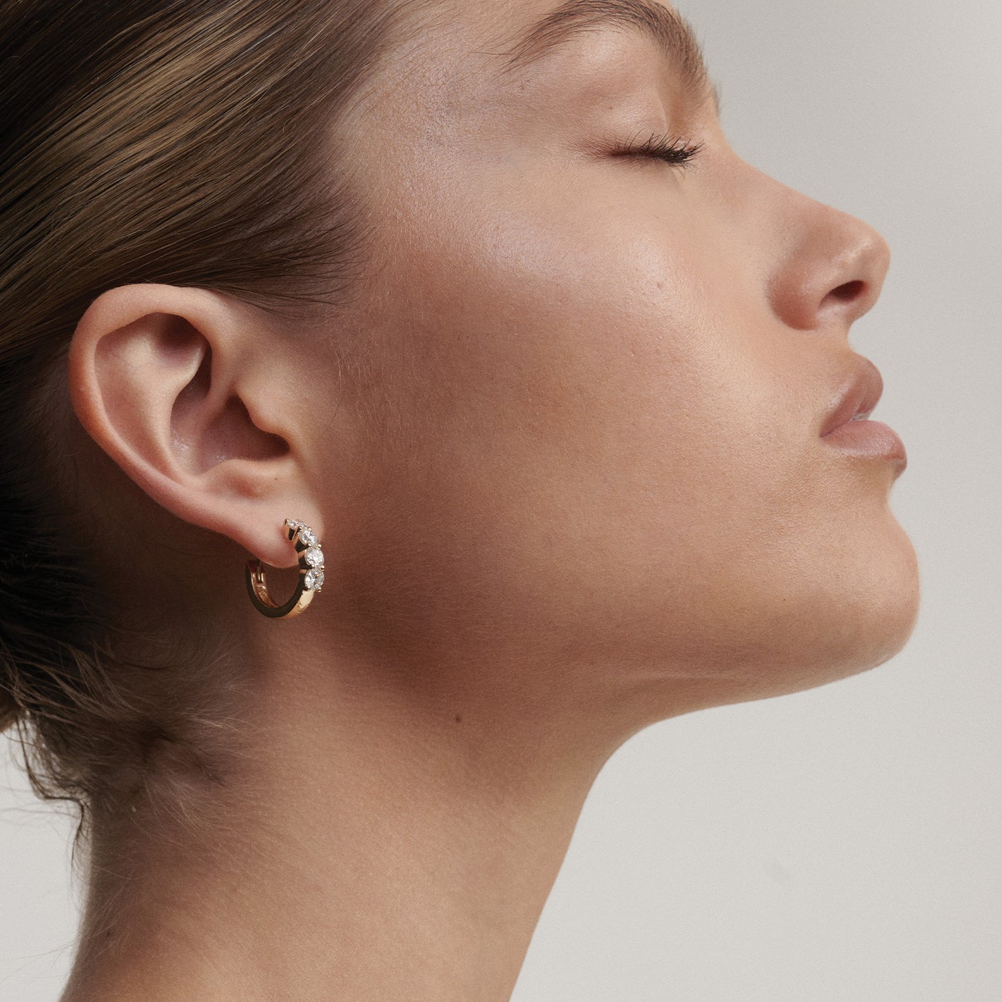 Close-up of a person wearing a gold hoop earring with small stones on a neutral background