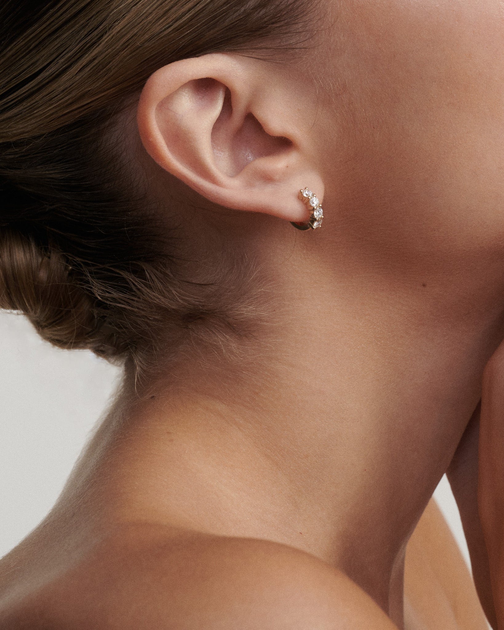 Close-up of a woman wearing a diamond earring. [text overlay: Signature Diamond Huggies]