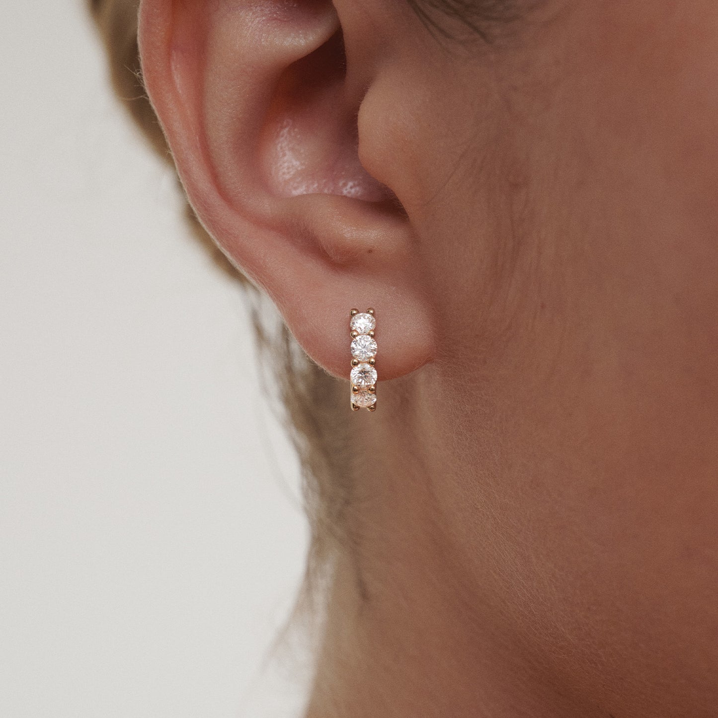 Close-up of an ear wearing a set of diamond hoop earrings on a neutral background