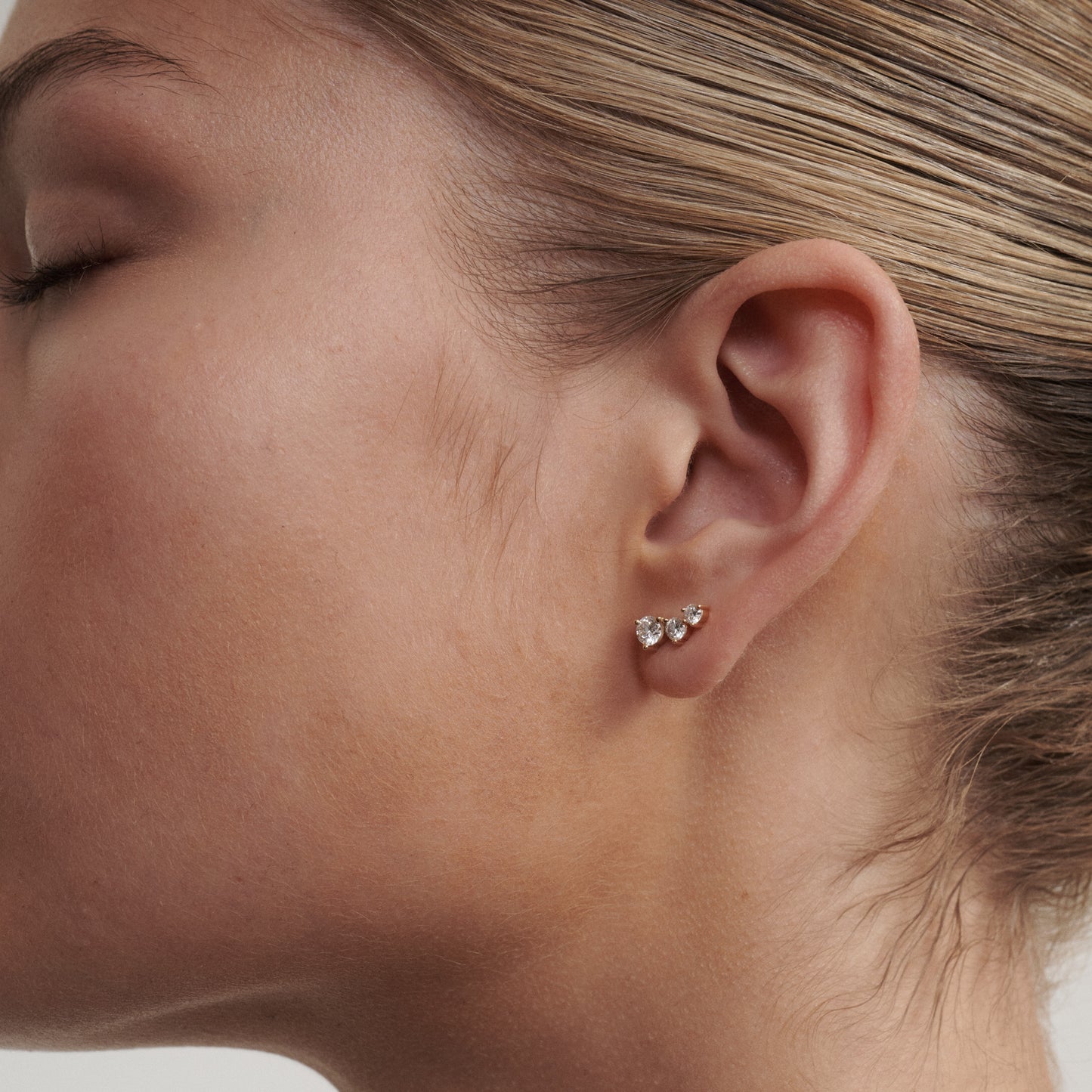 Close-up of a person wearing diamond stud earrings with a neutral background