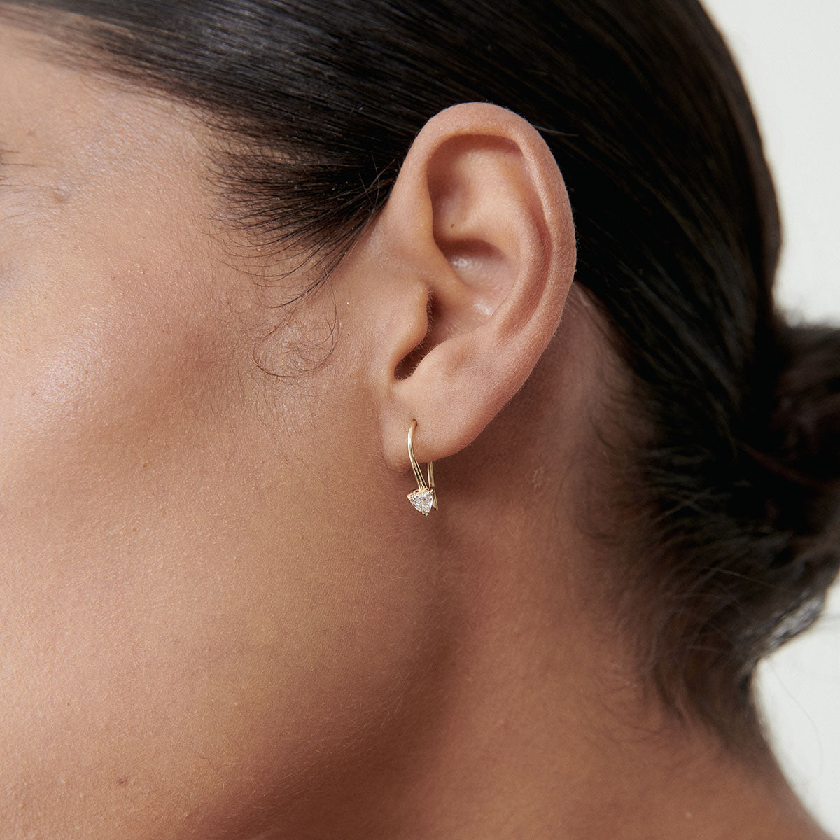 Close-up of a woman's ear wearing a gold hoop earring with a delicate diamond pendant, showcasing luxury jewellery elegance.