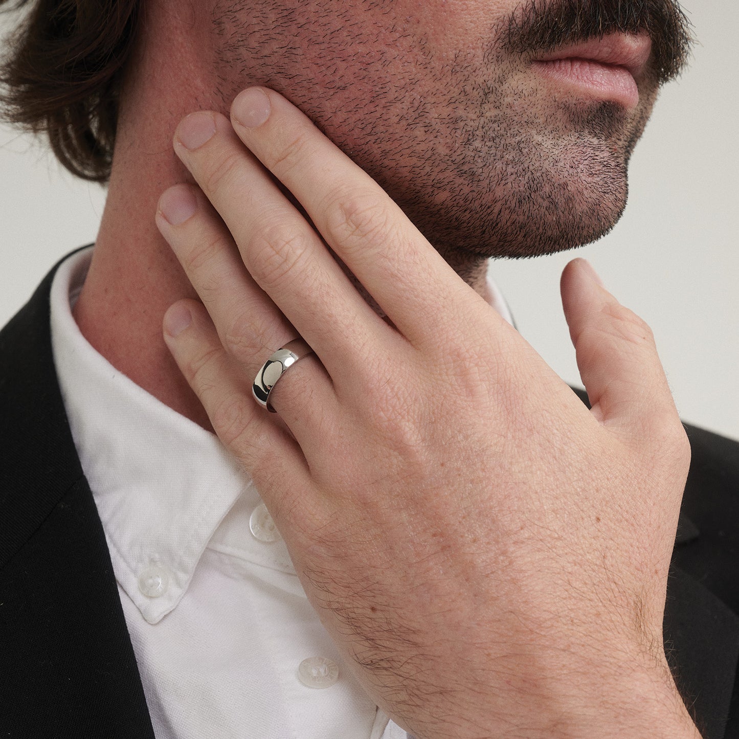 Close-up of a man's hand with a ring touching his chin against a neutral background