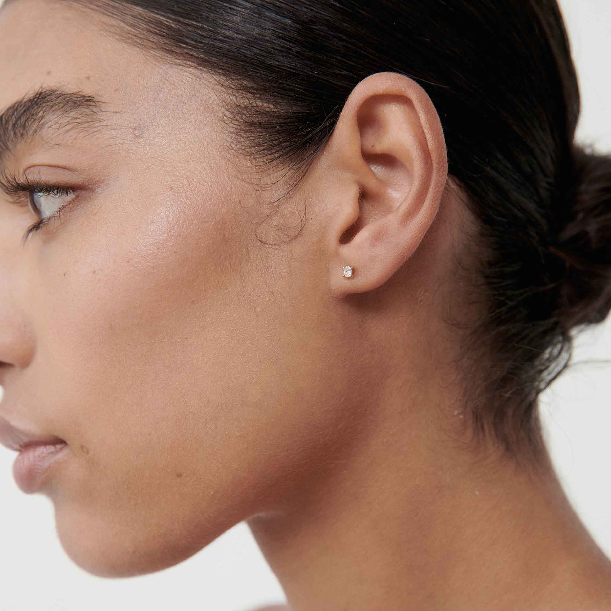 Close-up of woman’s ear wearing a small diamond stud earring; smooth complexion, minimalist high-end jewellery style.
