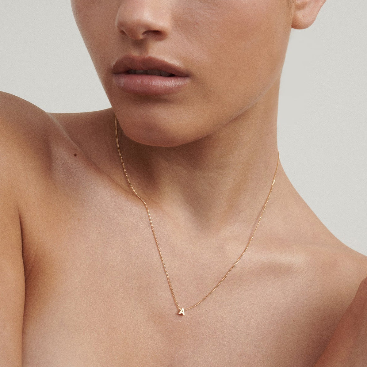 Woman wearing a delicate gold necklace against a neutral background