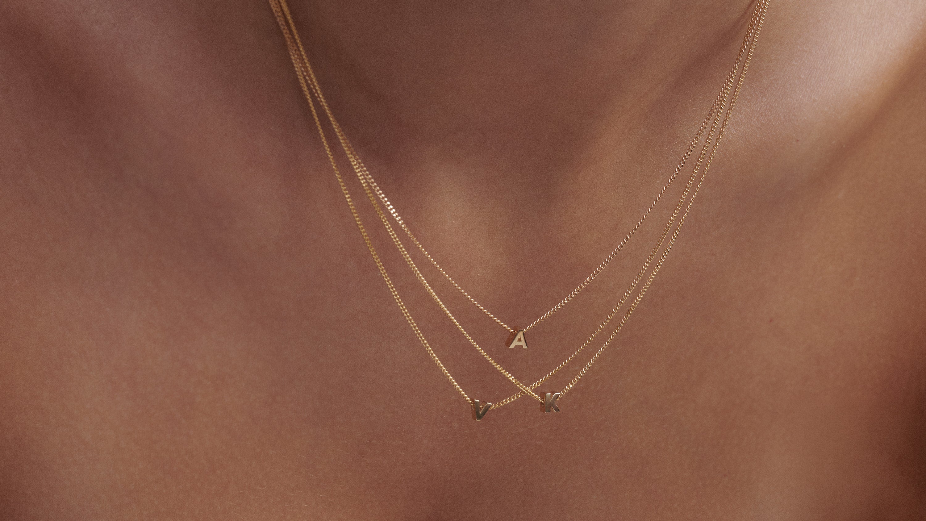 Close-up of a woman wearing three layered Tiny Letter Charm Necklace in 9ct yellow gold.