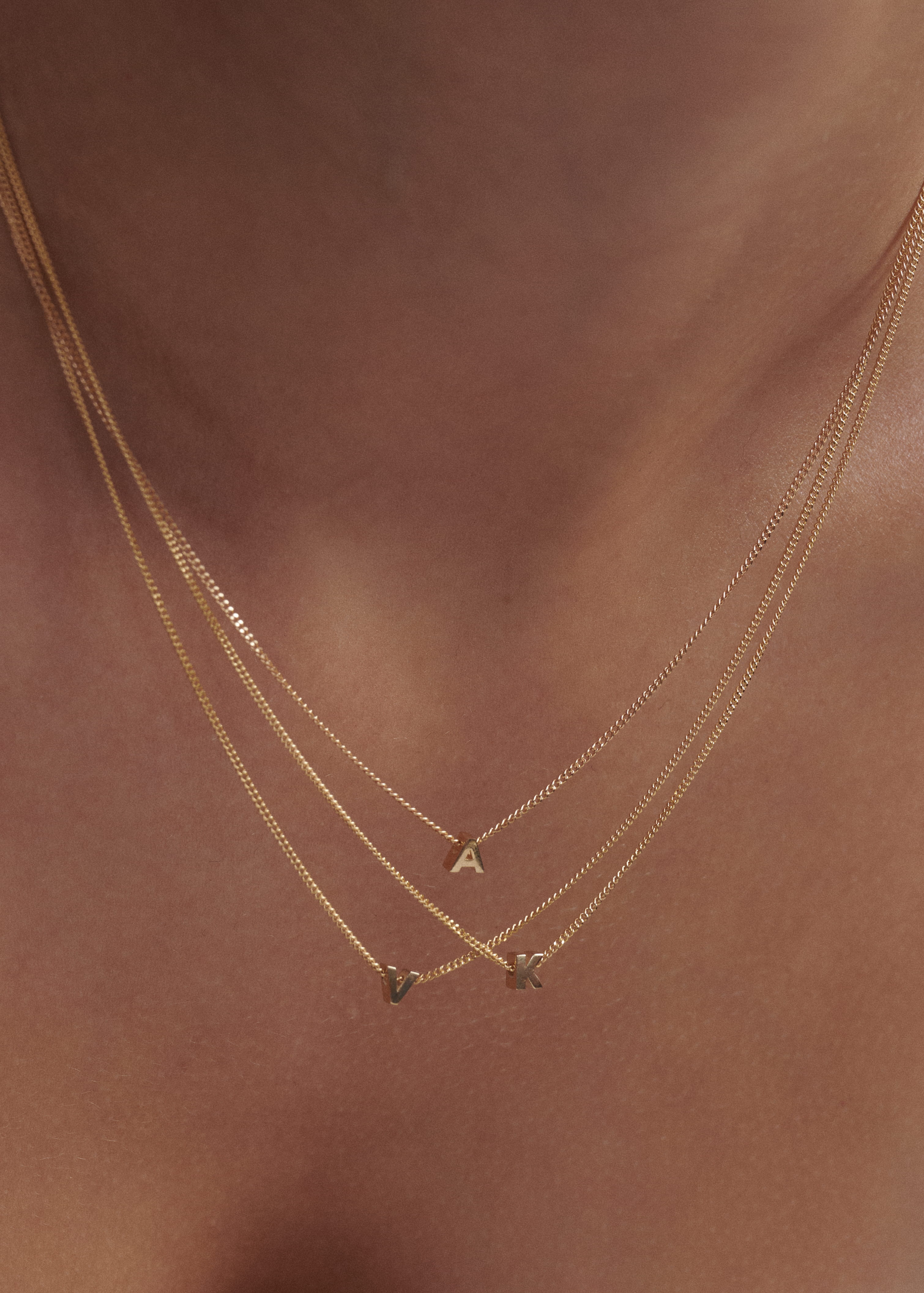 Close-up of a woman wearing three layered Tiny Letter Charm Necklace in 9ct yellow gold.