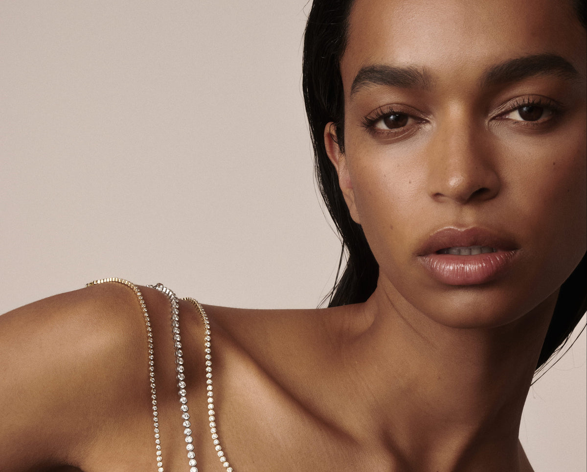 Model wearing yellow gold bezel-set lab-grown diamond tennis jewellery draped over her shoulder by Kate & Kole