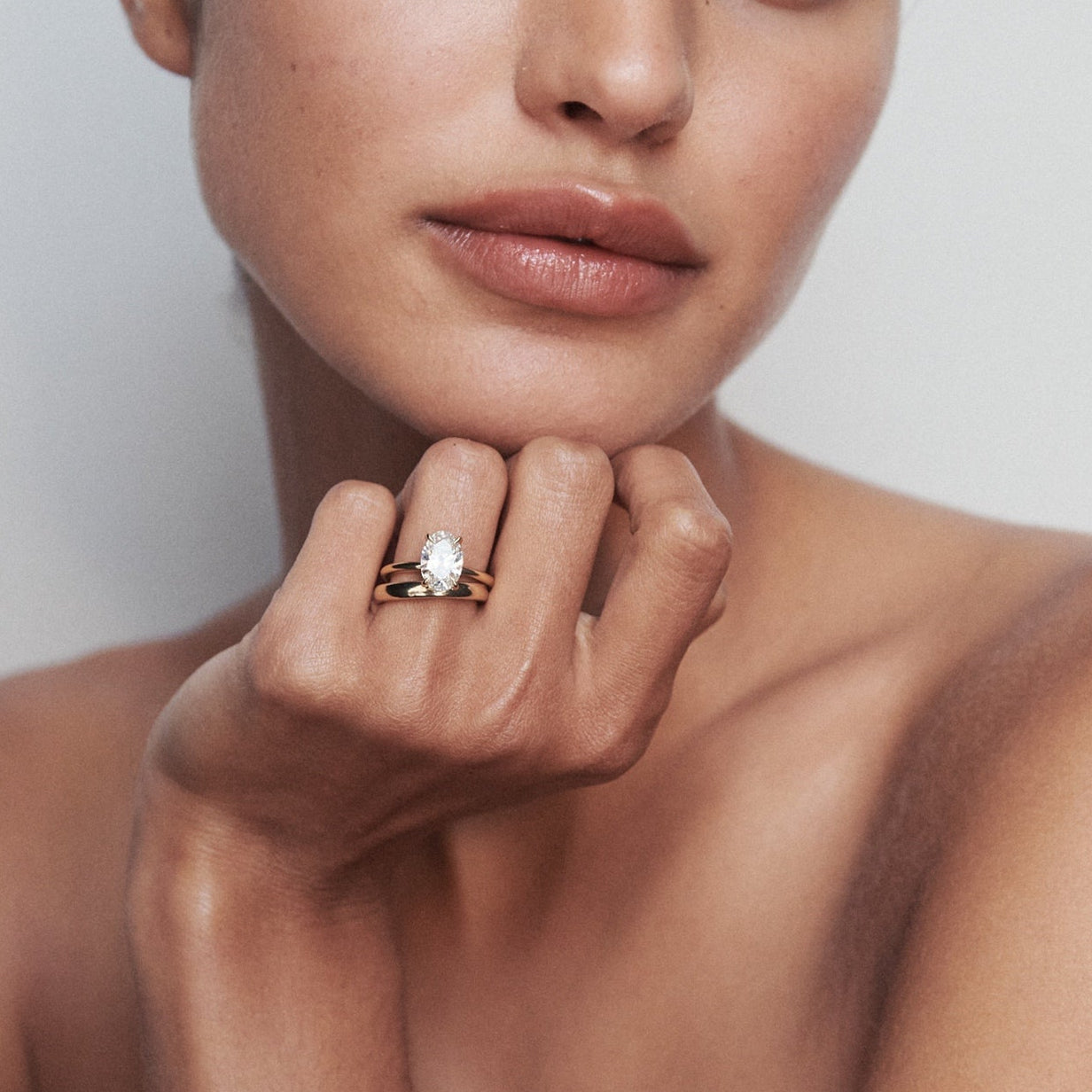 Woman with sleek hair, showcasing a luxurious gold ring with a large pearl, against a soft, neutral background. Elegant jewellery display.