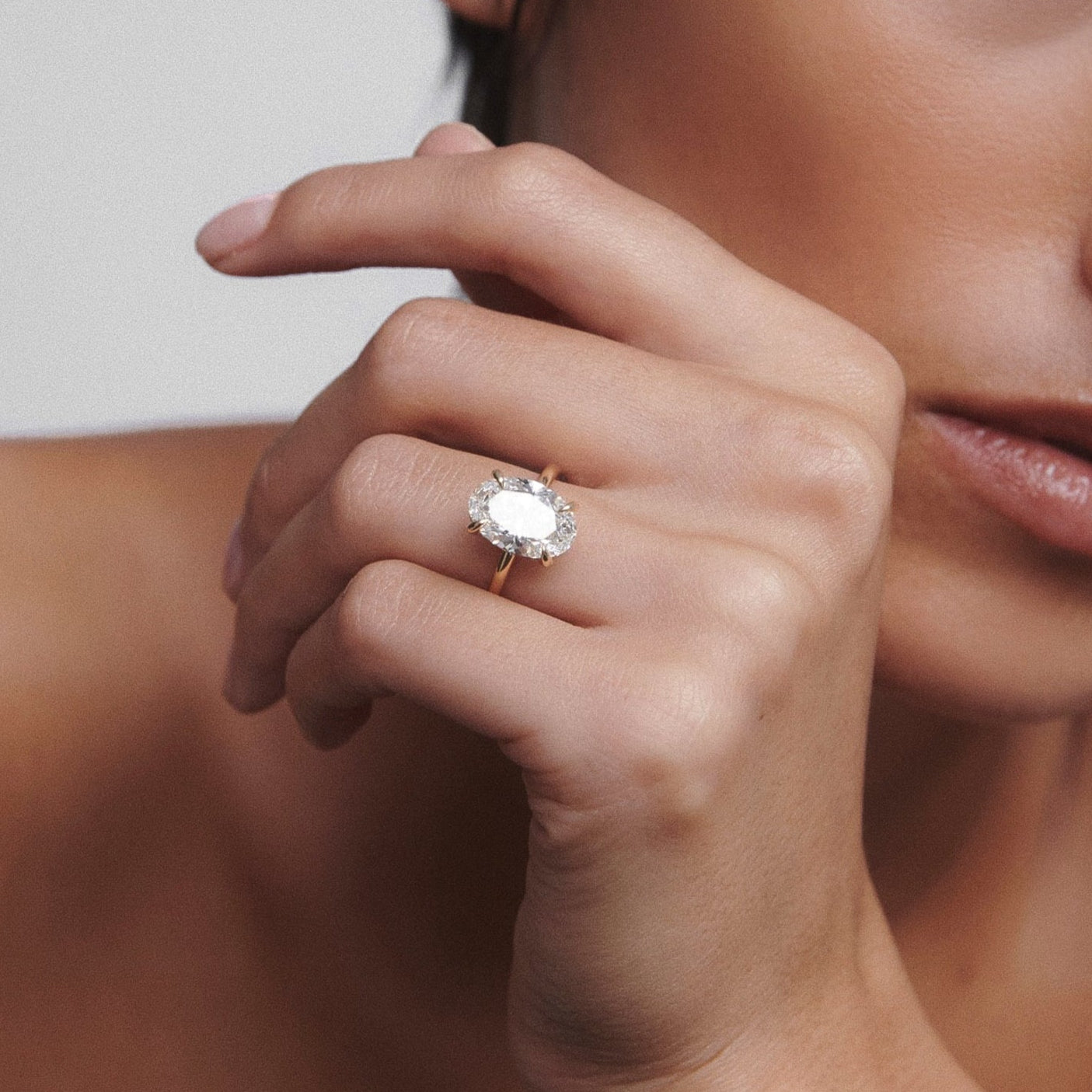 Woman showcasing an elegant, large oval diamond ring; bare shoulders, neutral background. Luxury jewellery focus.