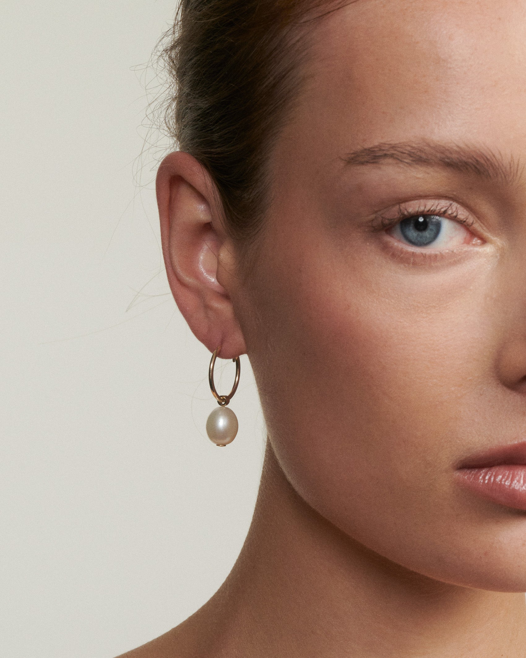 Close-up of a woman wearing a pearl earring against a neutral background