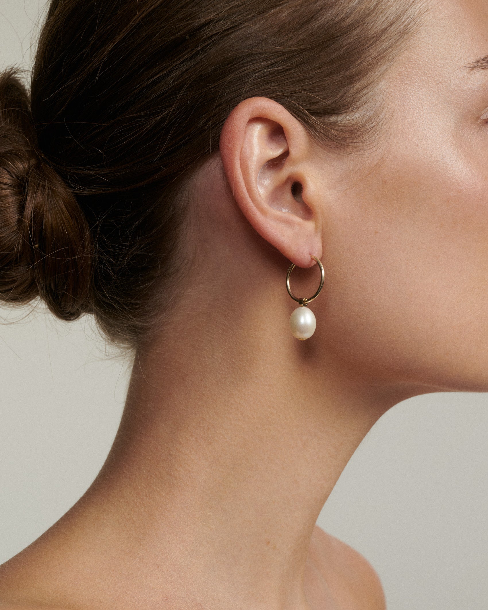 Close-up of a person wearing a pearl earring with a neutral background