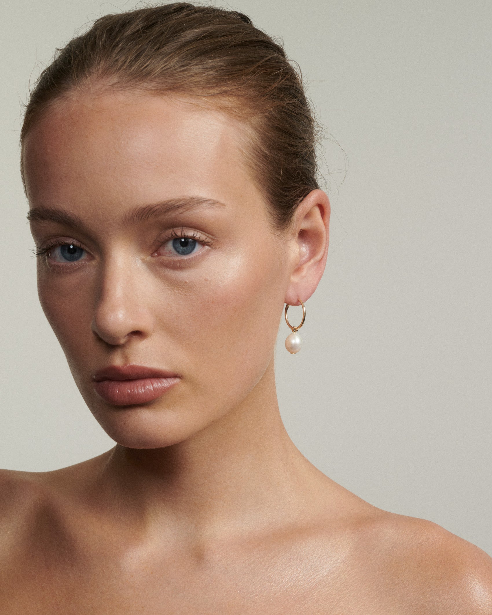 Woman wearing gold hoop earrings with a pearl accent on a neutral background