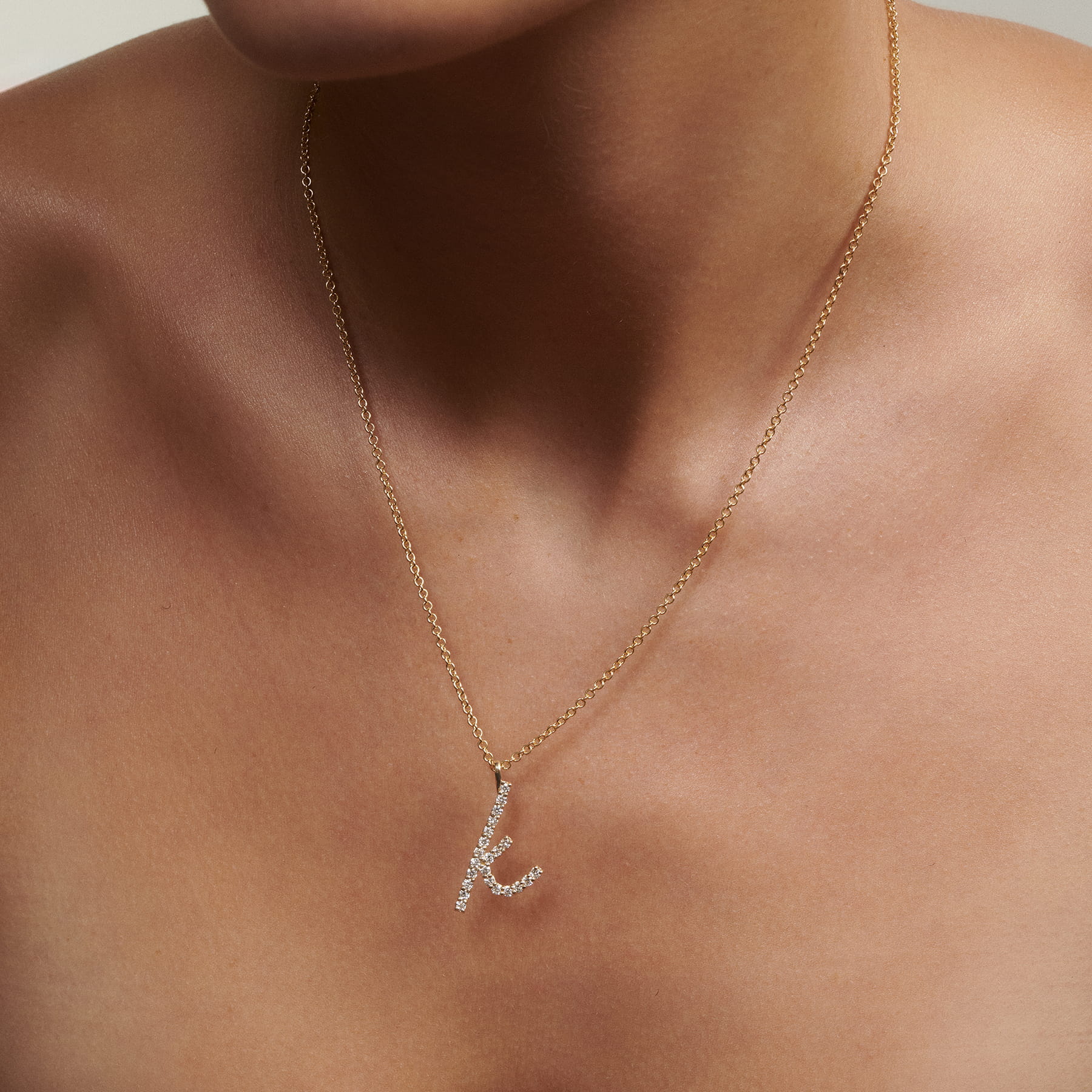 Close up of woman wearing Script Diamond Letter K Necklace in gold