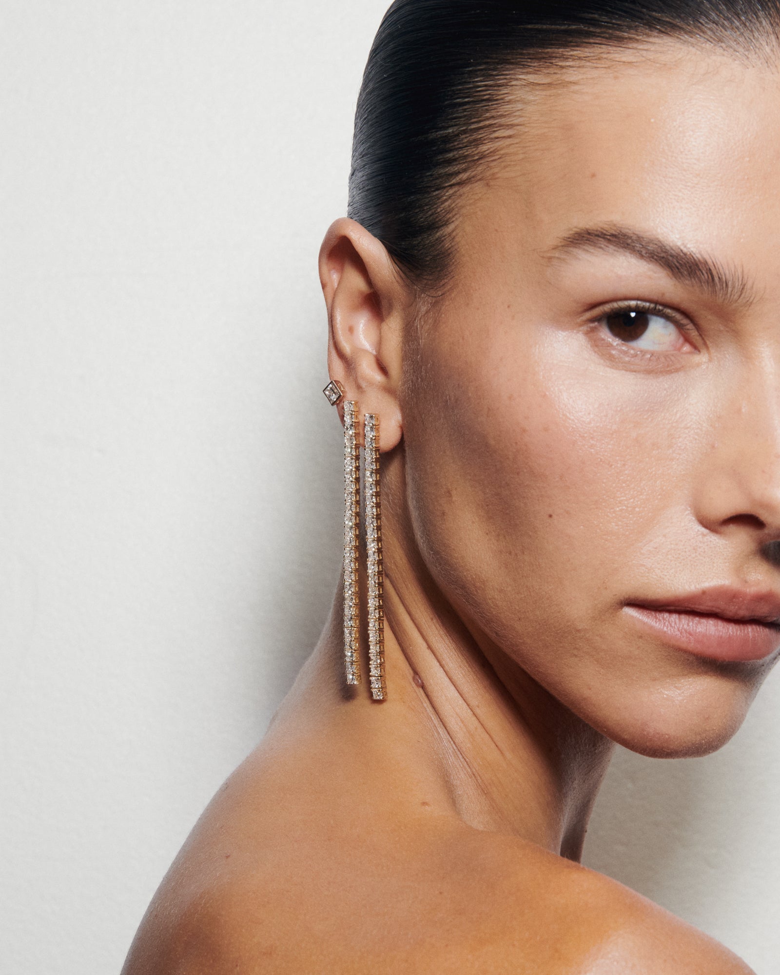 Close-up of a woman wearing long, dangling earrings with a neutral background