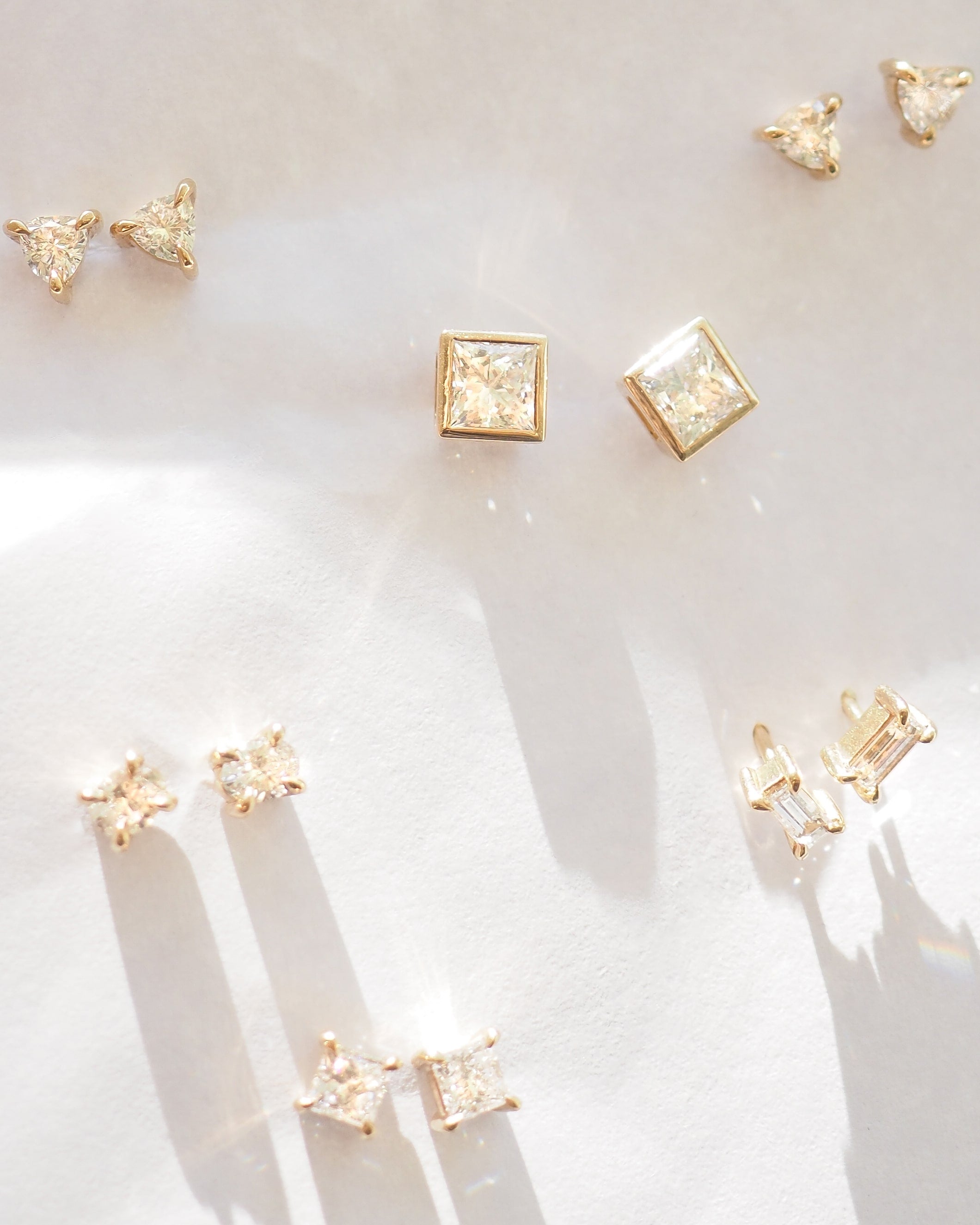 Assortment of Kate & Kole lab-grown diamond stud earrings in various cuts, set in yellow gold on a light surface.