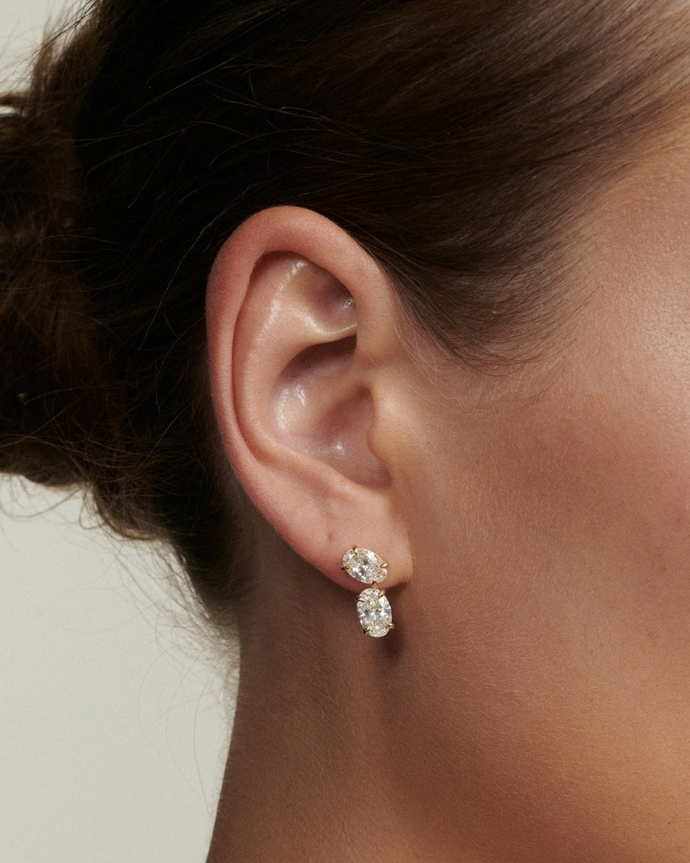Close-up of an ear wearing a diamond earring with a neutral background