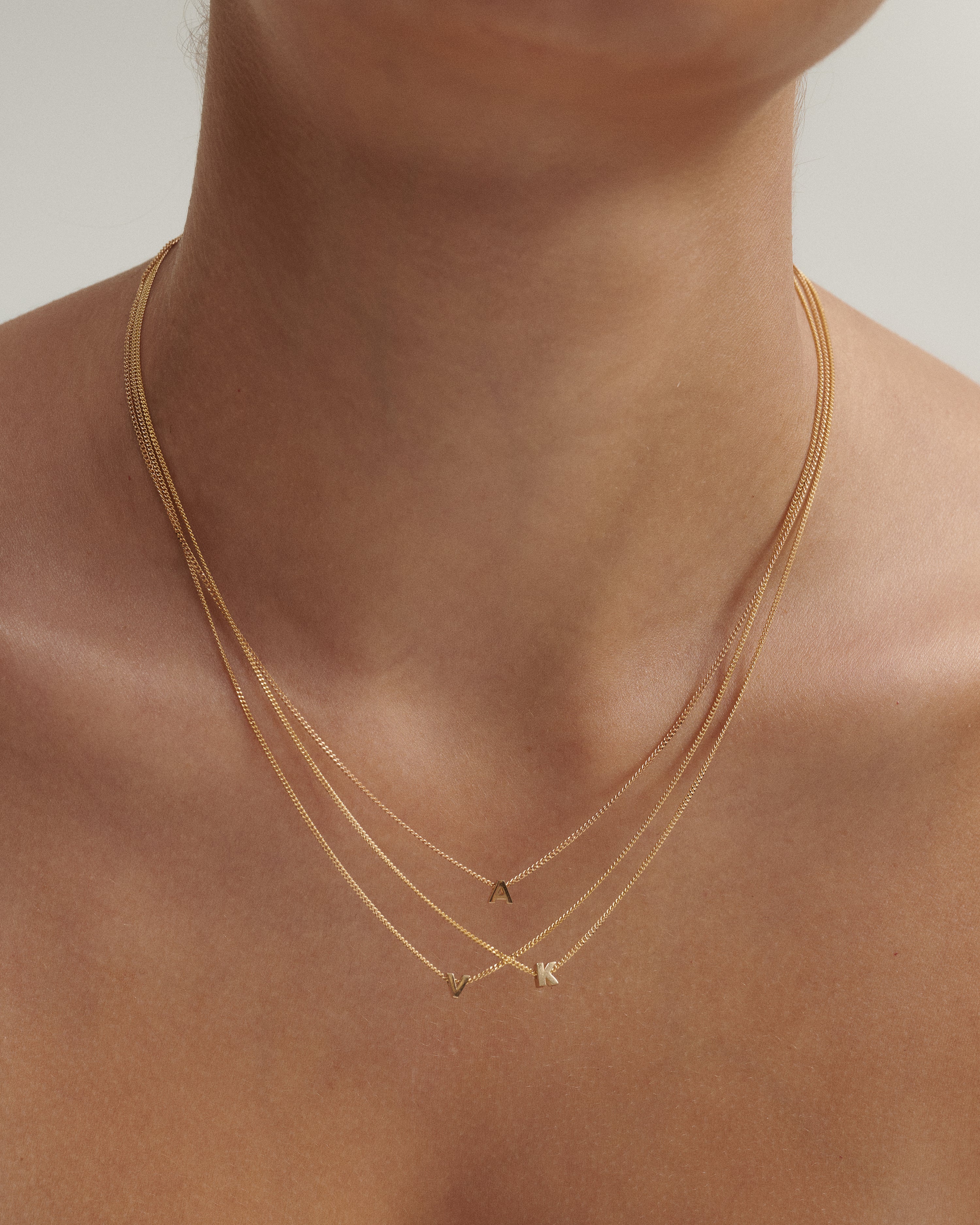Gold necklaces with letter pendants on a person's neck against a neutral background
