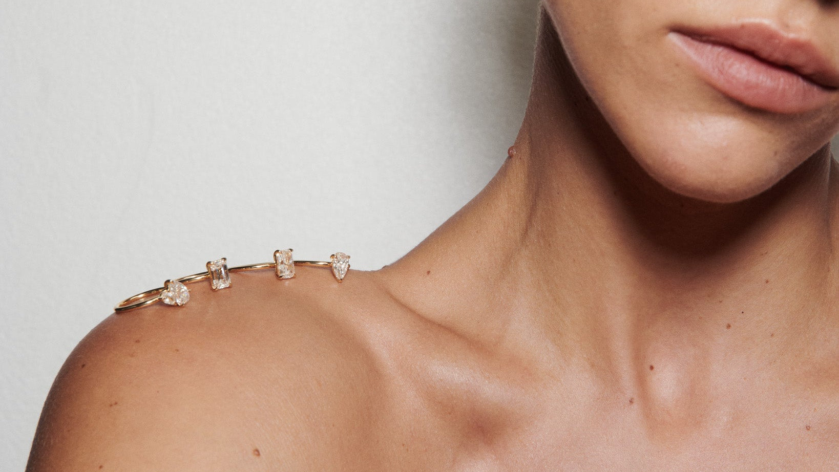 Close-up of a person with four engagement rings sitting balanced on their shoulder against a neutral background