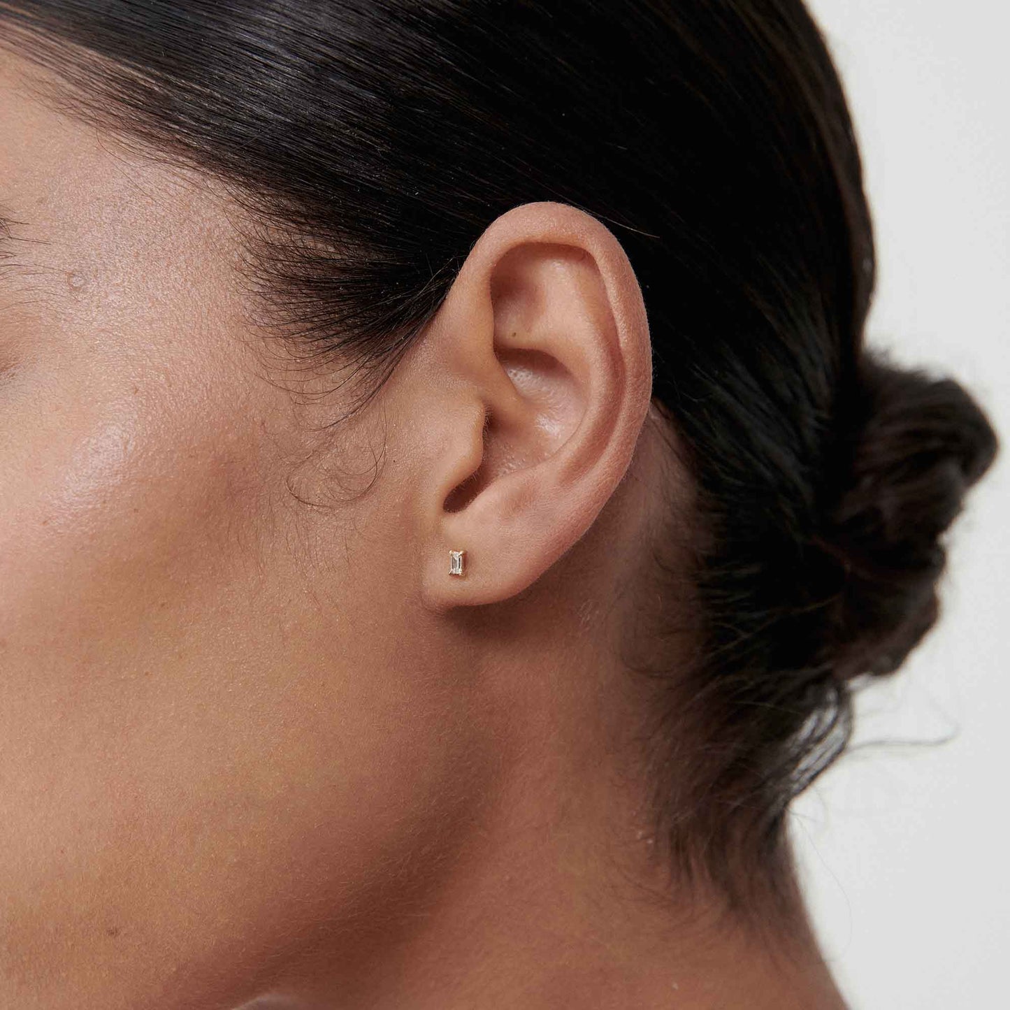 Close-up of a woman's ear adorned with a delicate gold and diamond stud earring. Hair tied back, showcasing luxury jewellery.