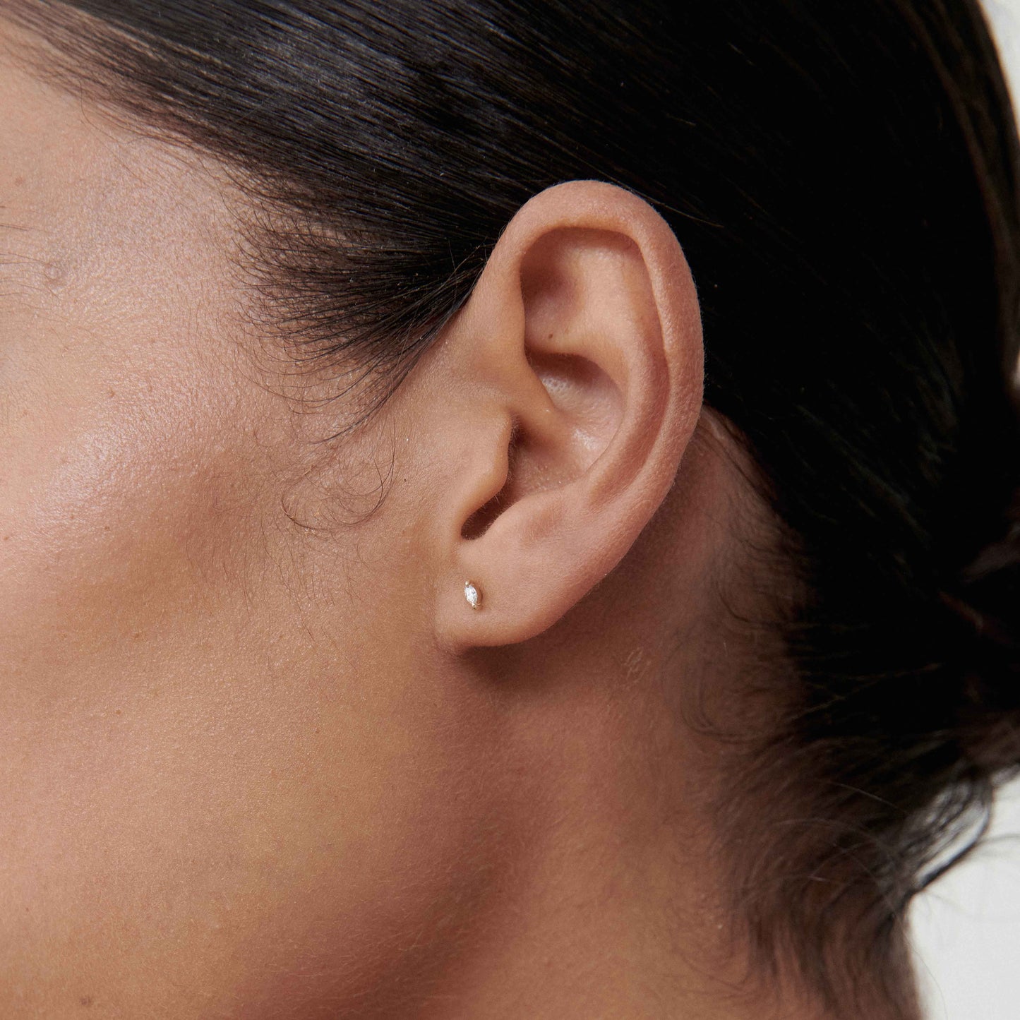 Close-up of a woman's ear wearing a small, elegant gold stud earring, showcasing minimalist luxury jewellery fashion.