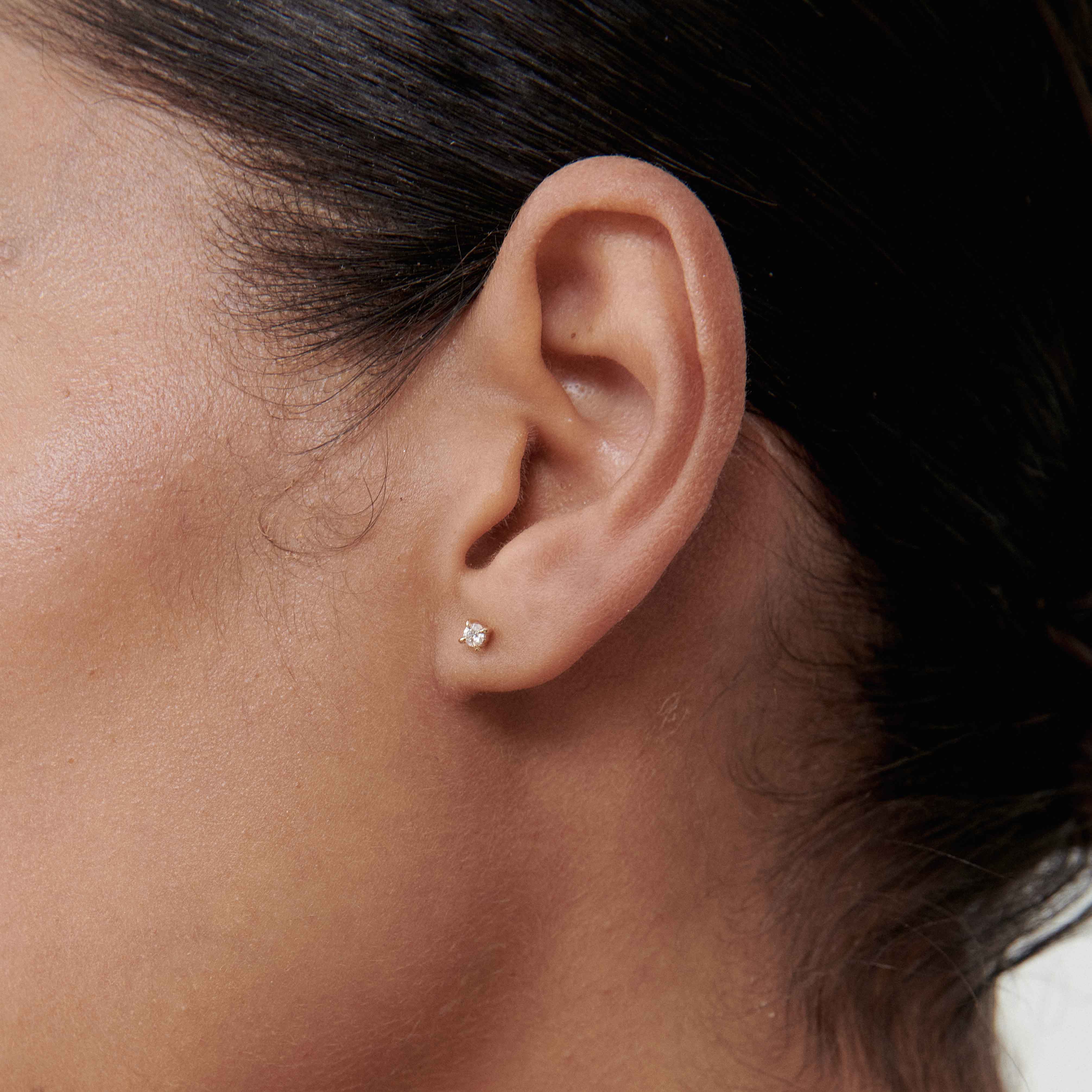 Close-up of a woman's ear wearing a small, elegant diamond stud earring on smooth, tanned skin.