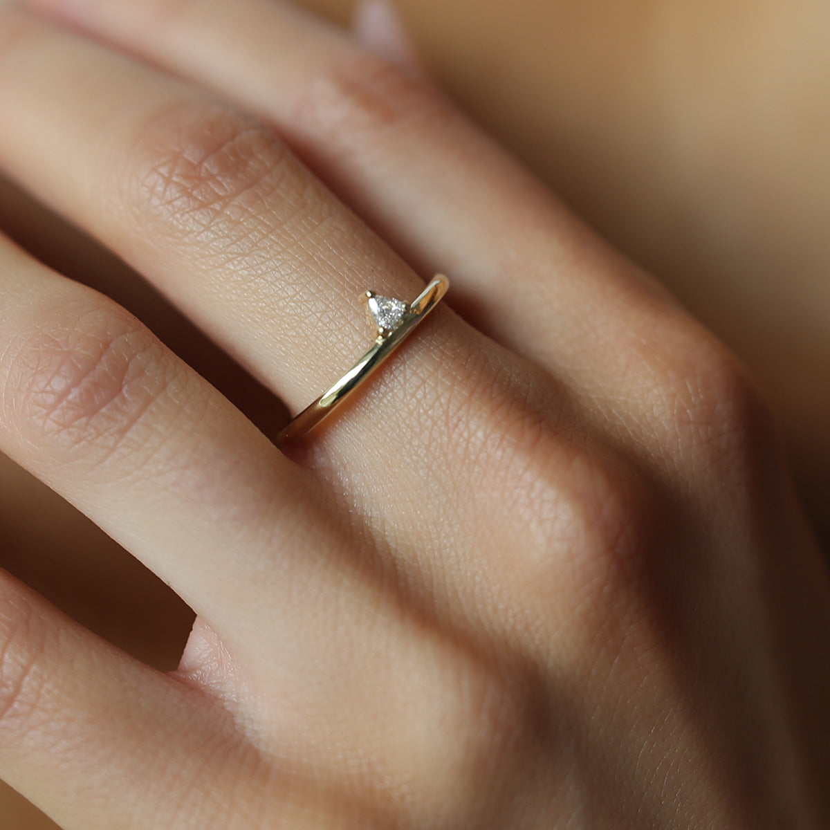 Gold ring with a small, triangle-cut diamond on a woman's hand, highlighting luxury jewellery design and elegance.