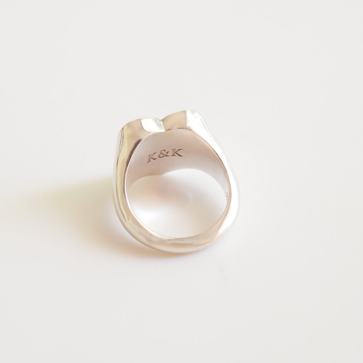 Silver ring with 'K&K' engraving on a light gray background
