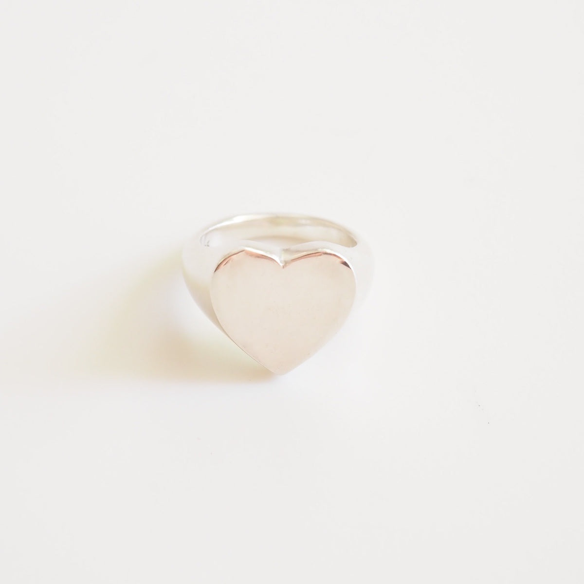Heart-shaped silver ring on a light beige background