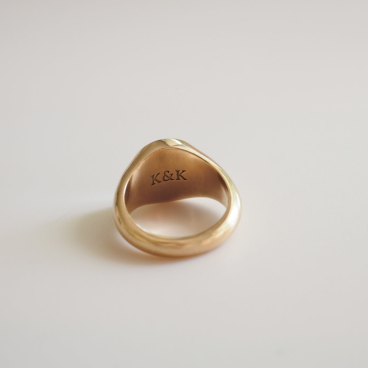 Gold ring with 'K&K' engraving on a light gray background