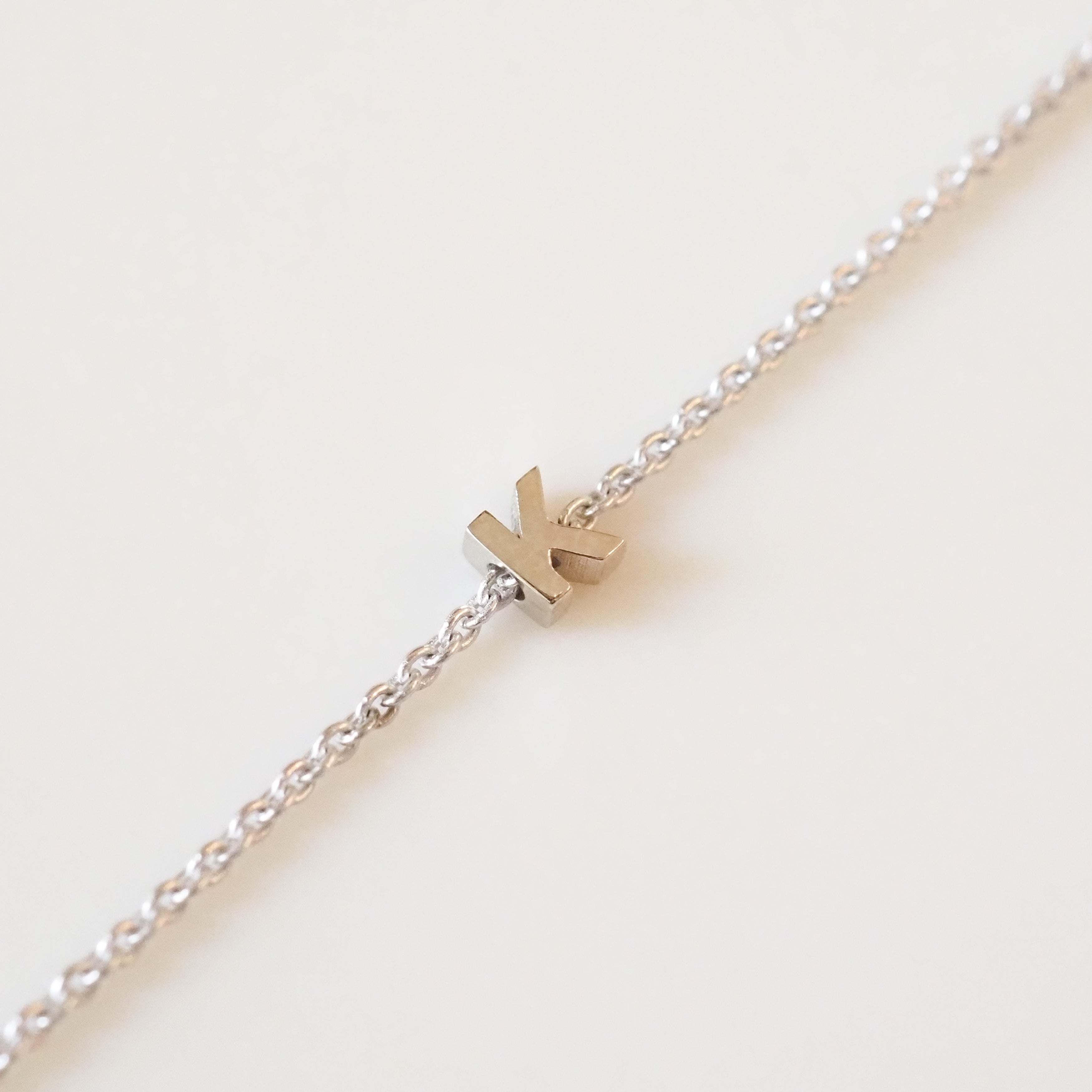 Gold 'K' charm on a silver chain against a light background
