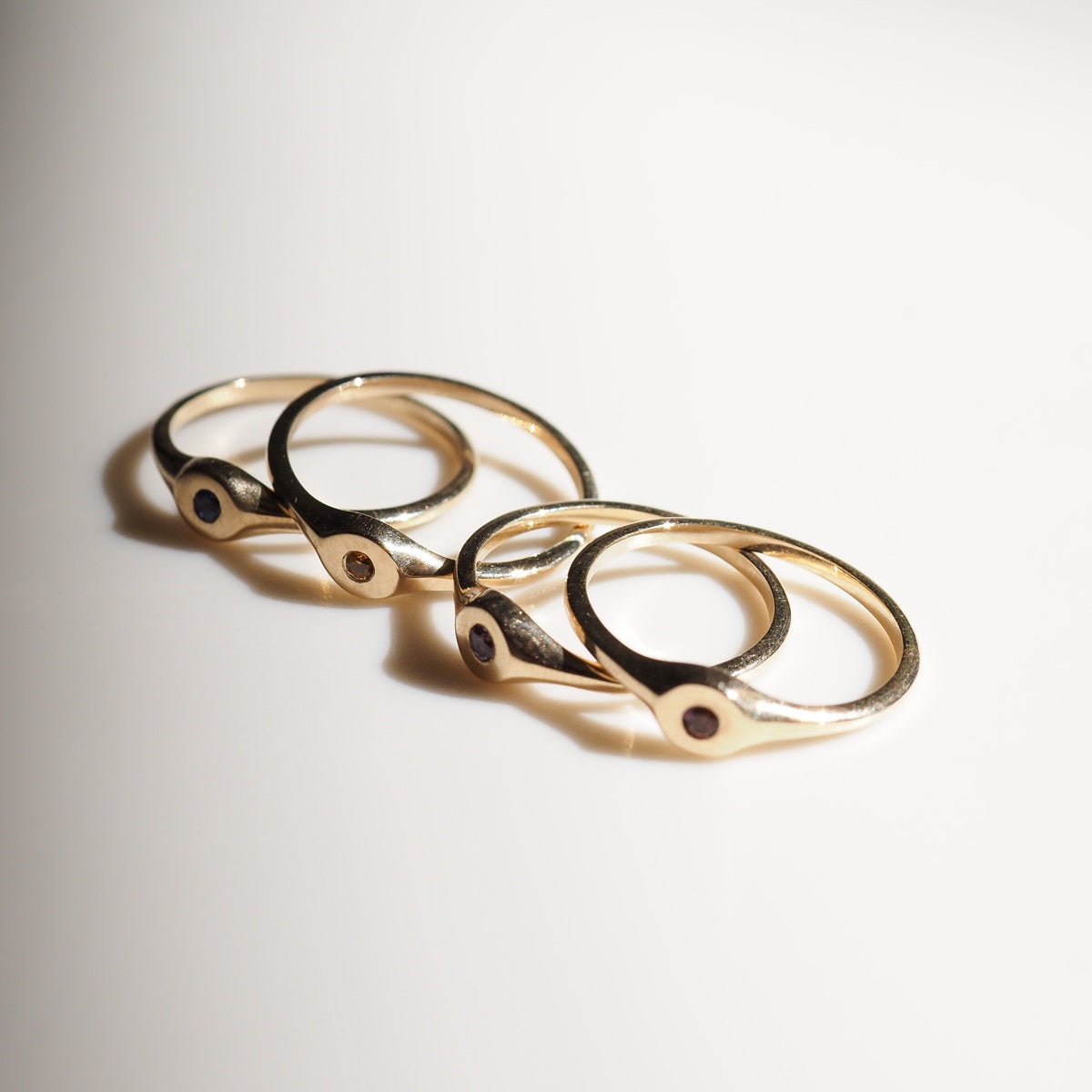 Four gold rings with gemstones on a light gray background