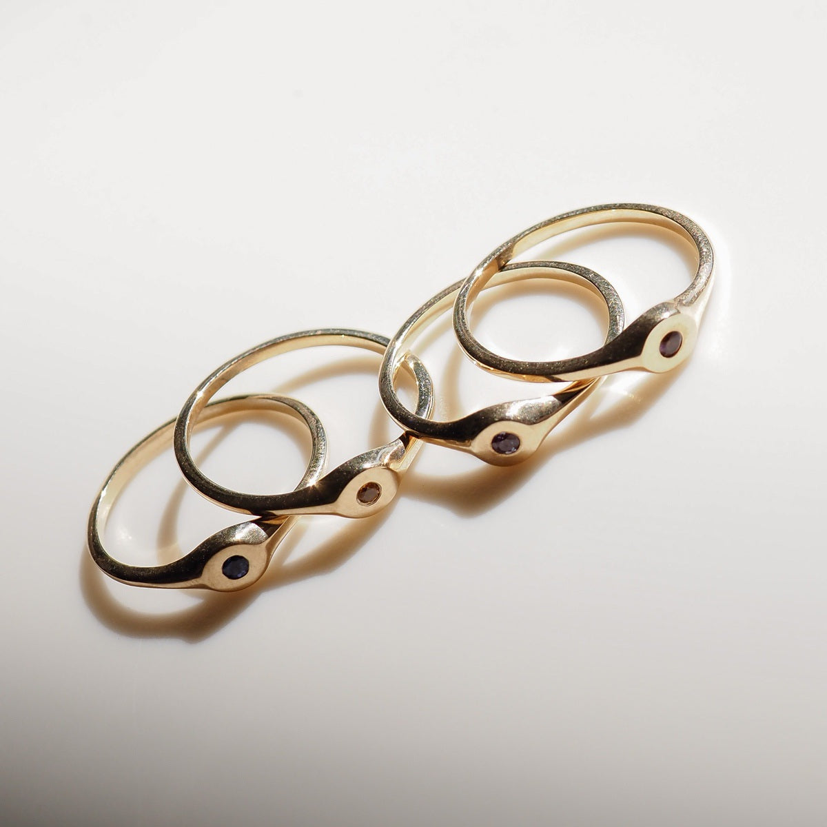 Four gold rings with gemstones on a light gray background