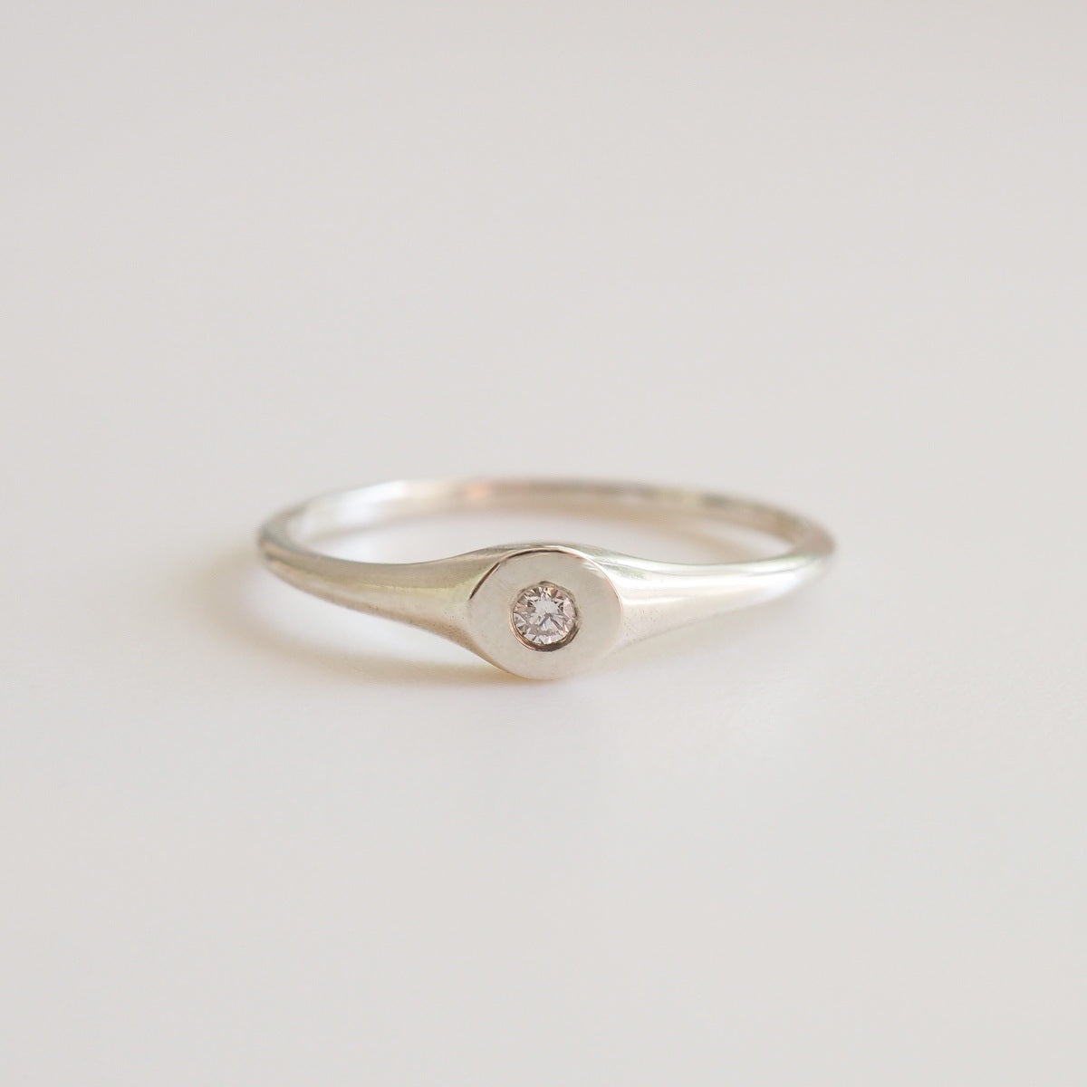 Silver ring with a small diamond on a light gray background