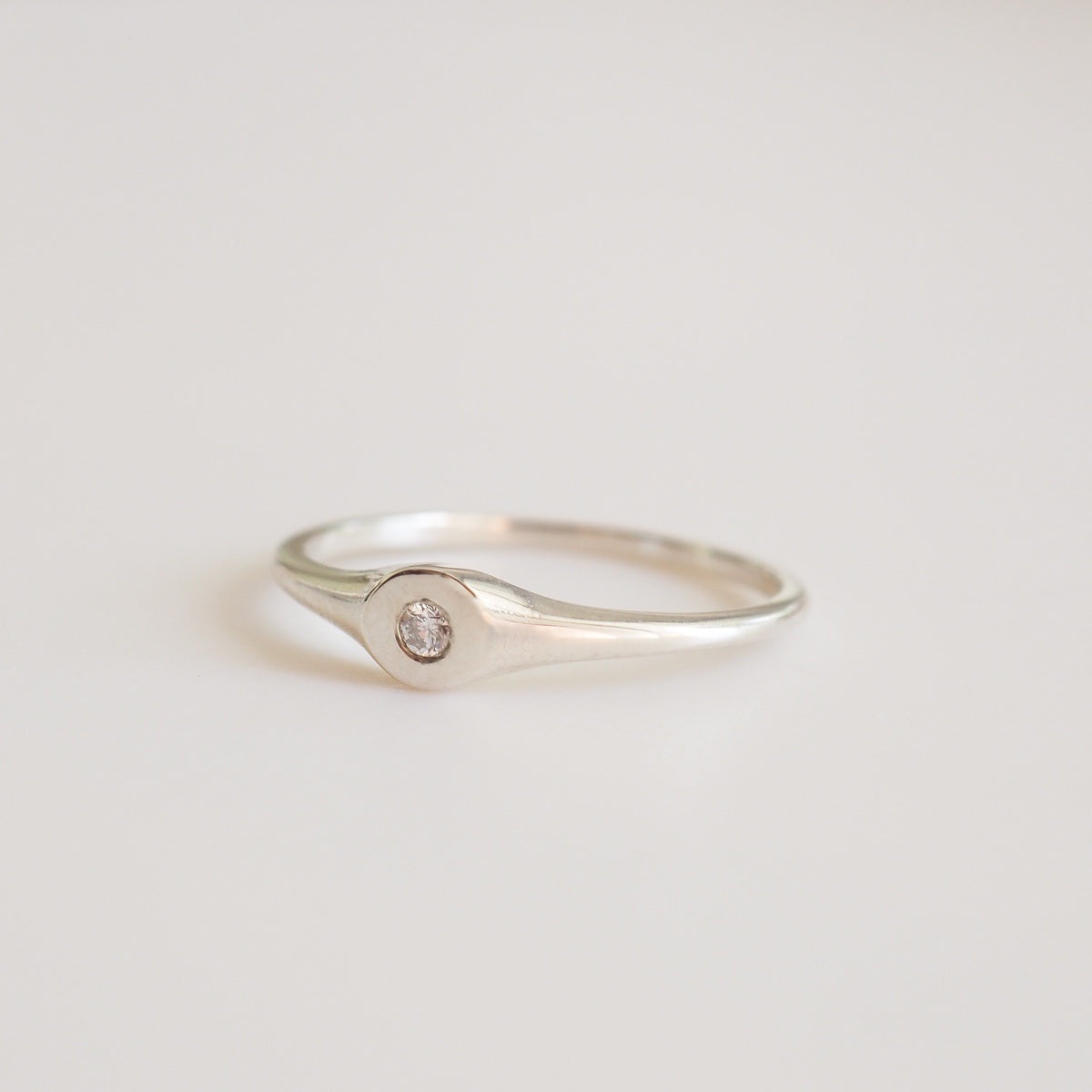 Silver ring with a small diamond on a light gray background
