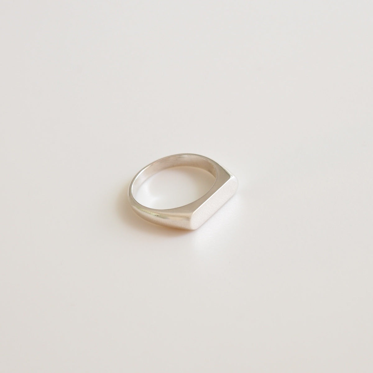 A flaylay of a narrow silver signet ring on a white background