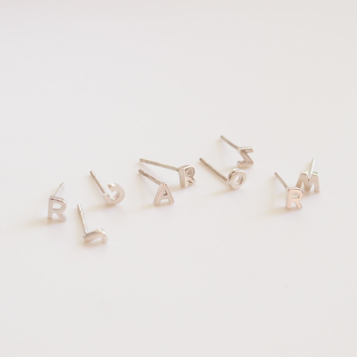 Multiple silver letter earrings on a light background