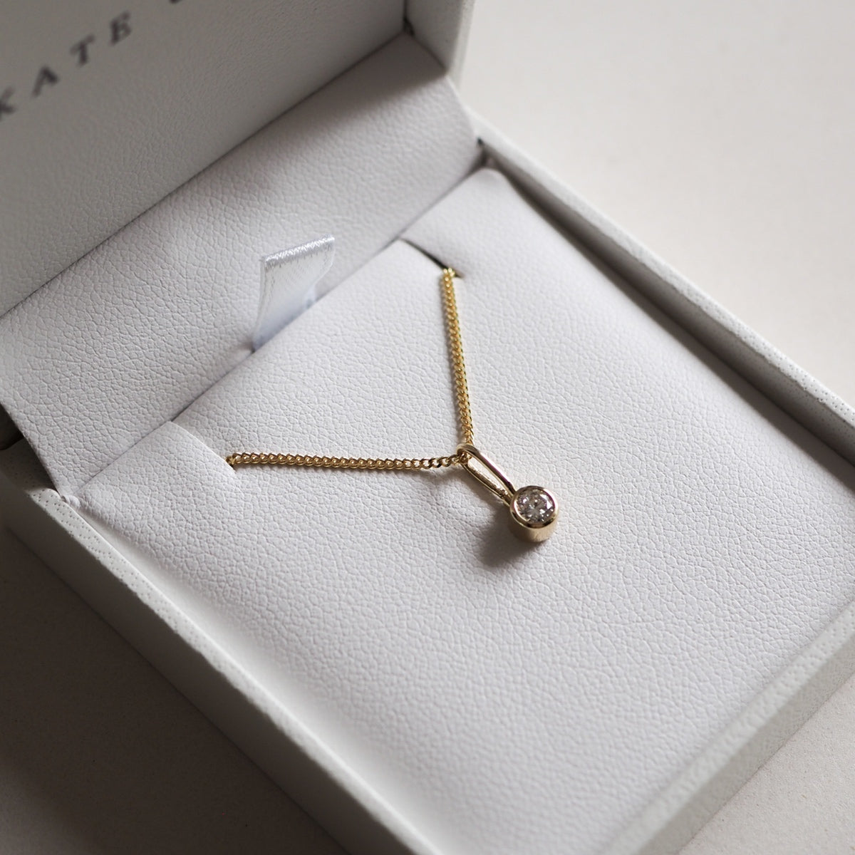 Gold necklace with a single diamond pendant in a white jewellery box, showcasing luxury and elegance suitable for a high-end style.