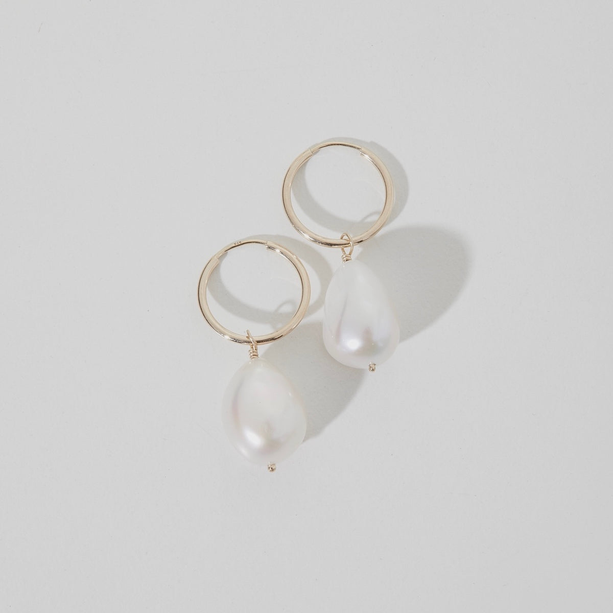 Flat lay of our solid gold small baroque pearl earrings in 9ct yellow gold on 15mm everyday sleepers.