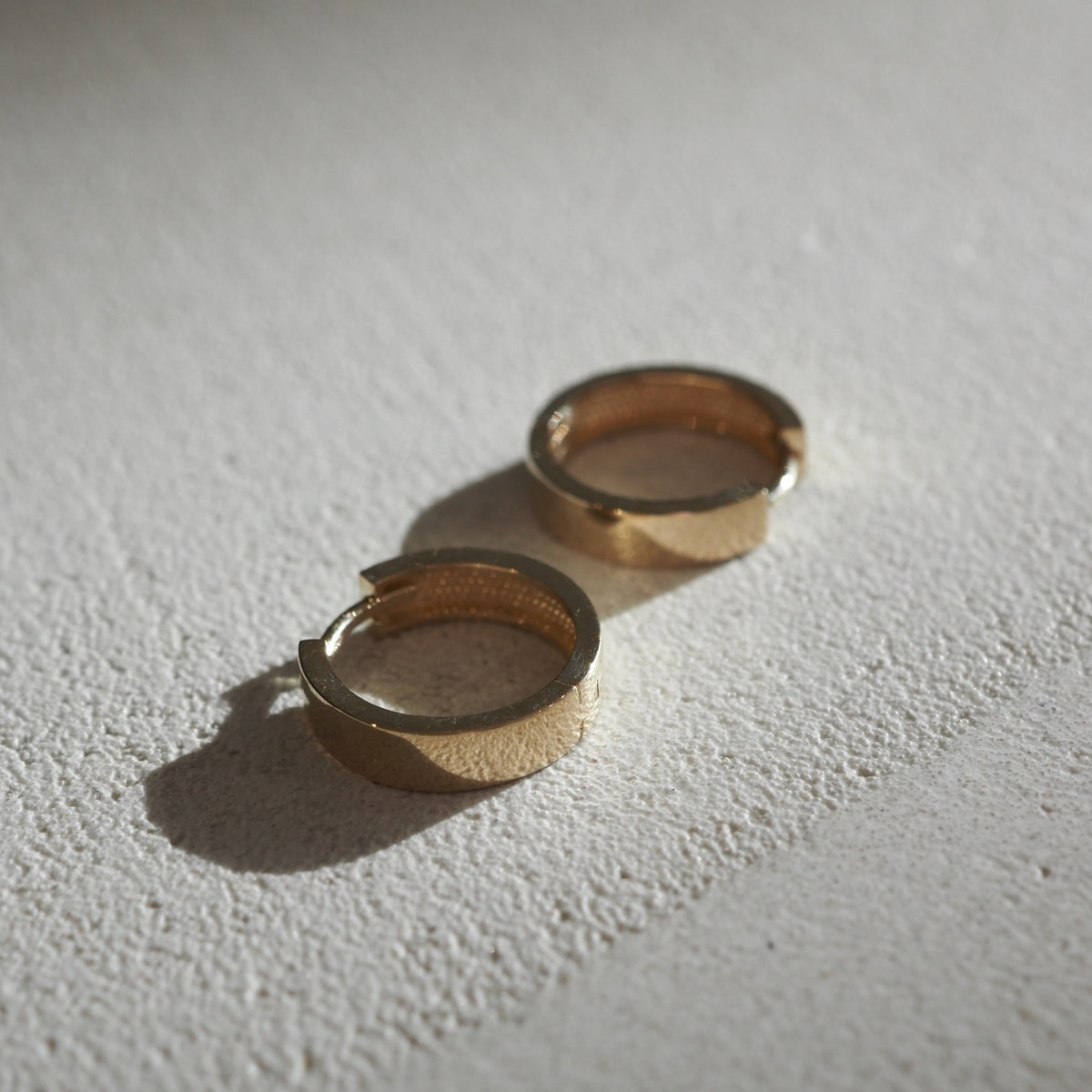 Solid Gold Huggies: Flat lay of small square hoop earrings made for everyday wear