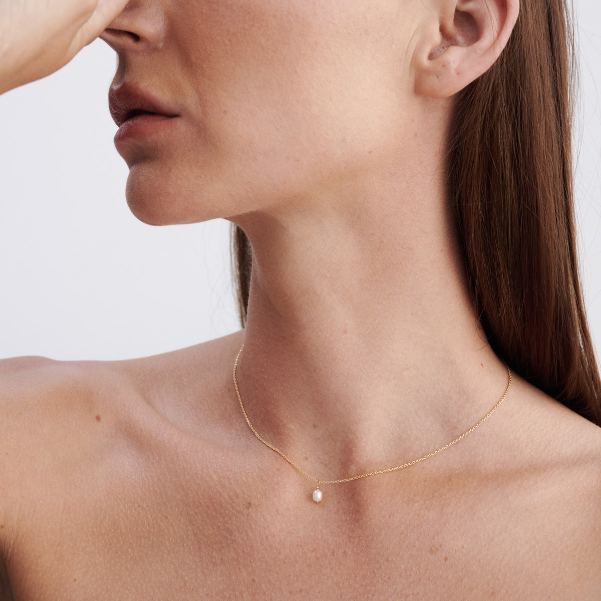 Close-up of a woman wearing a delicate gold necklace with a small pearl pendant, showcasing minimalist luxury jewellery.