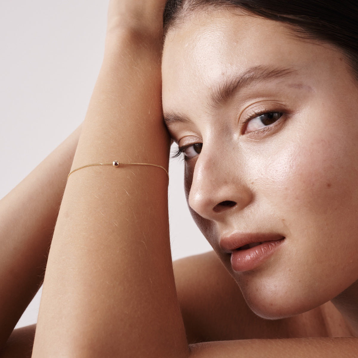 Model wears our 9ct Yellow Gold Tiny Birthstone Charm Bracelet with a personalised Ruby stone