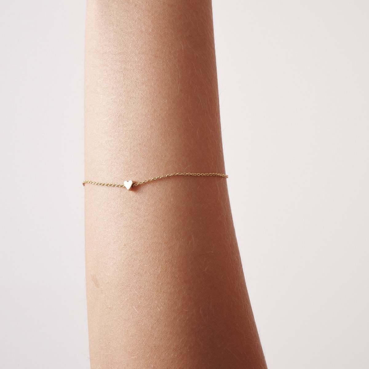 Solid Gold Tiny Heart Bracelet: Close up of a model wearing our 17cm 9ct yellow gold tiny heart bracelet